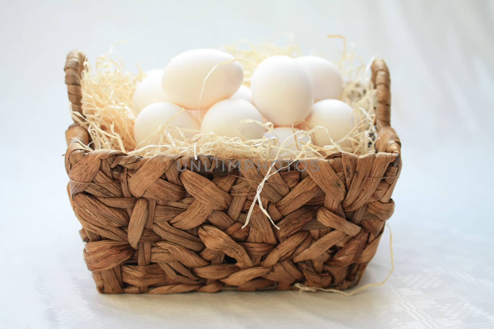 Wicker basket with hay and white eggs