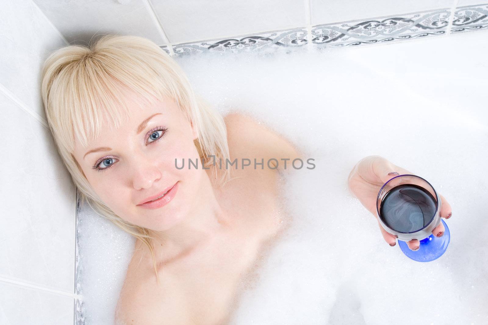 a young woman baths in a bathroom in much foam and drink wine.