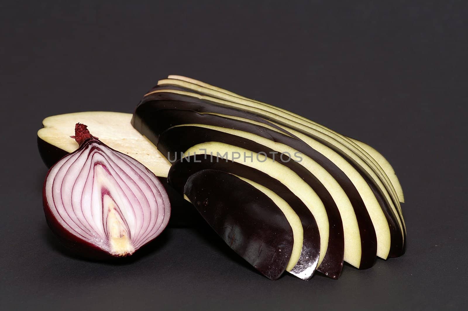 half of onion and sliced eggplant on black paper background