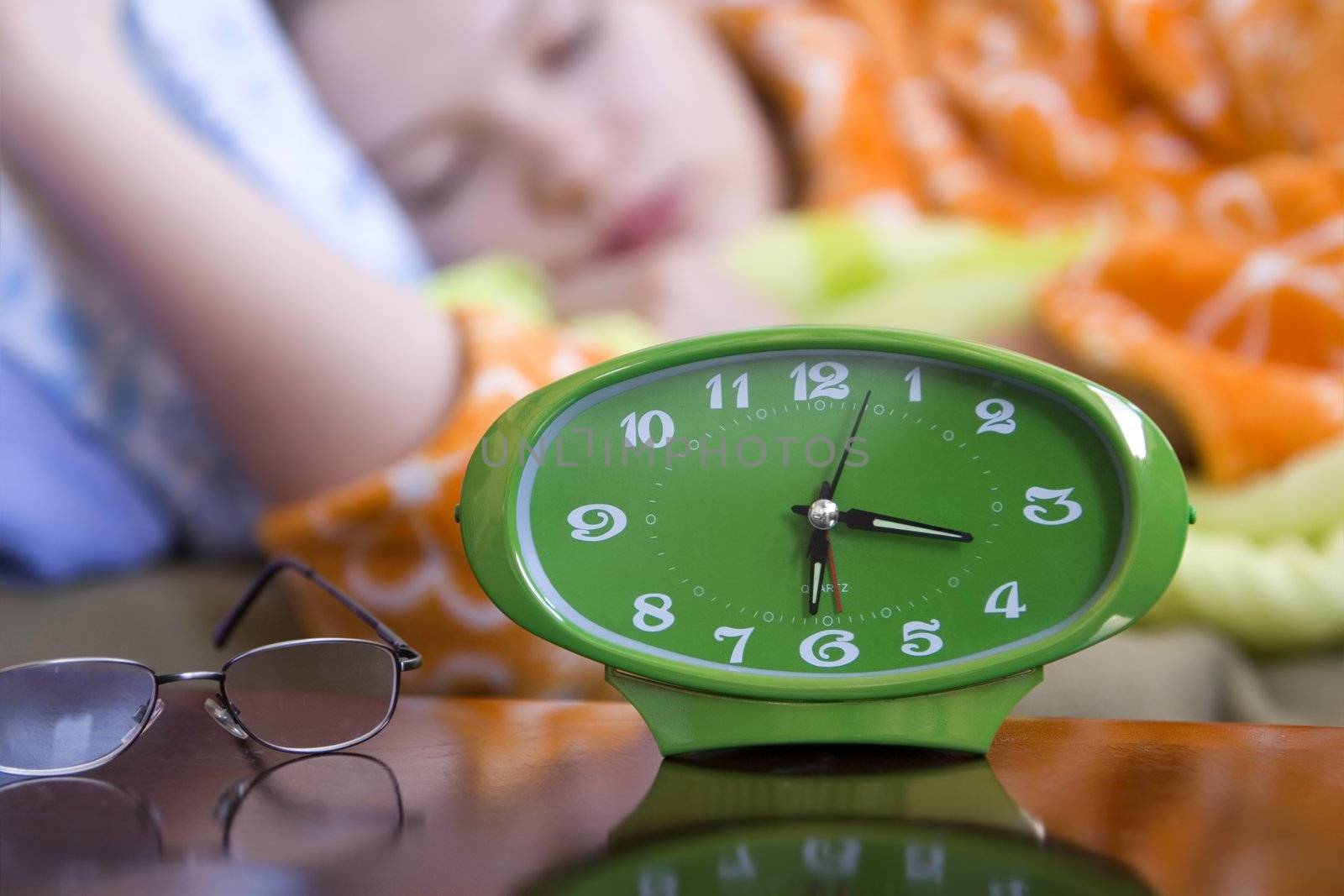 Green clock and glasses with a female sleeping in the background(shallow dof)