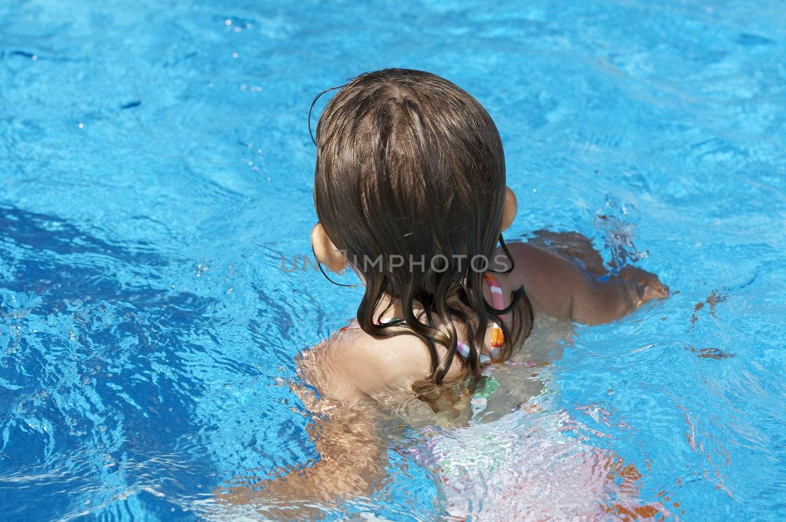 a cute little girl looking at pool water during the summer