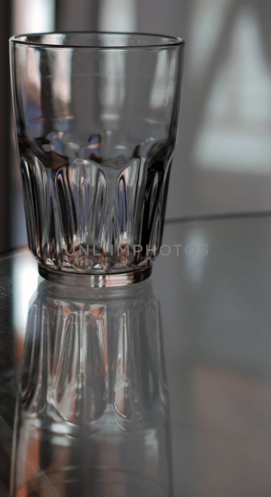 An empty glass sits with it's reflection on a glass table.