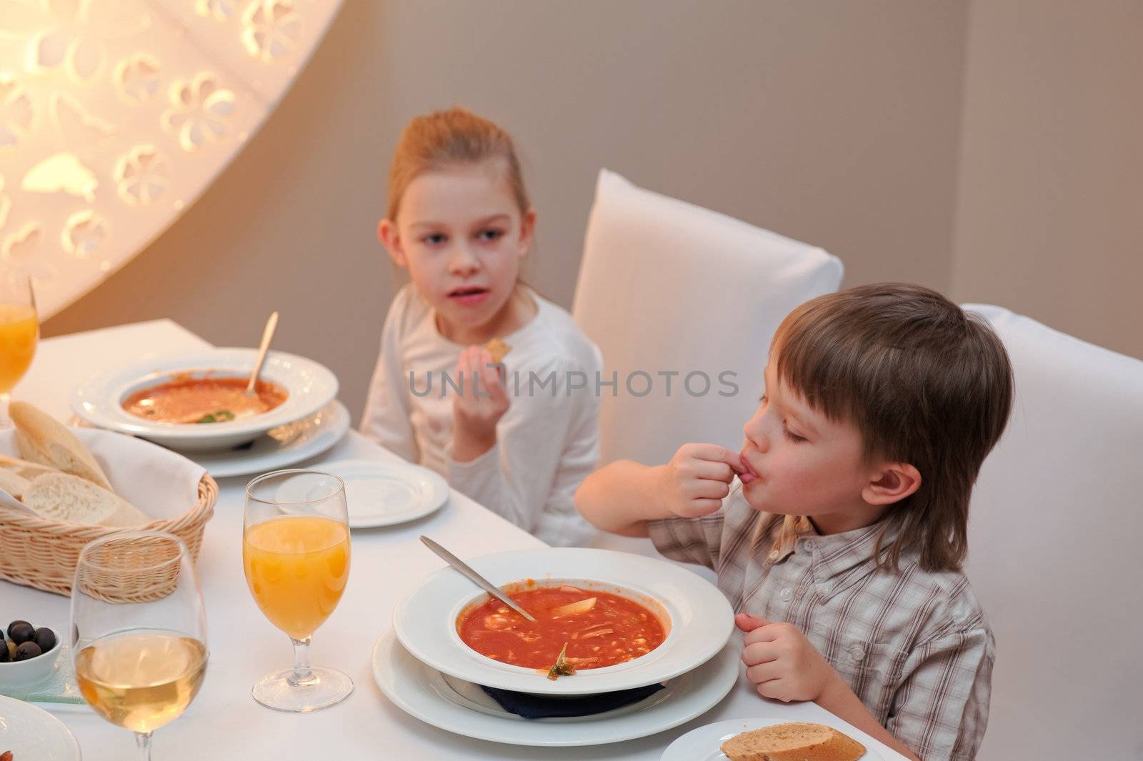 Sister and brother enjoying meal sitting at restaurant table. Boy in focus, girl out of focus.