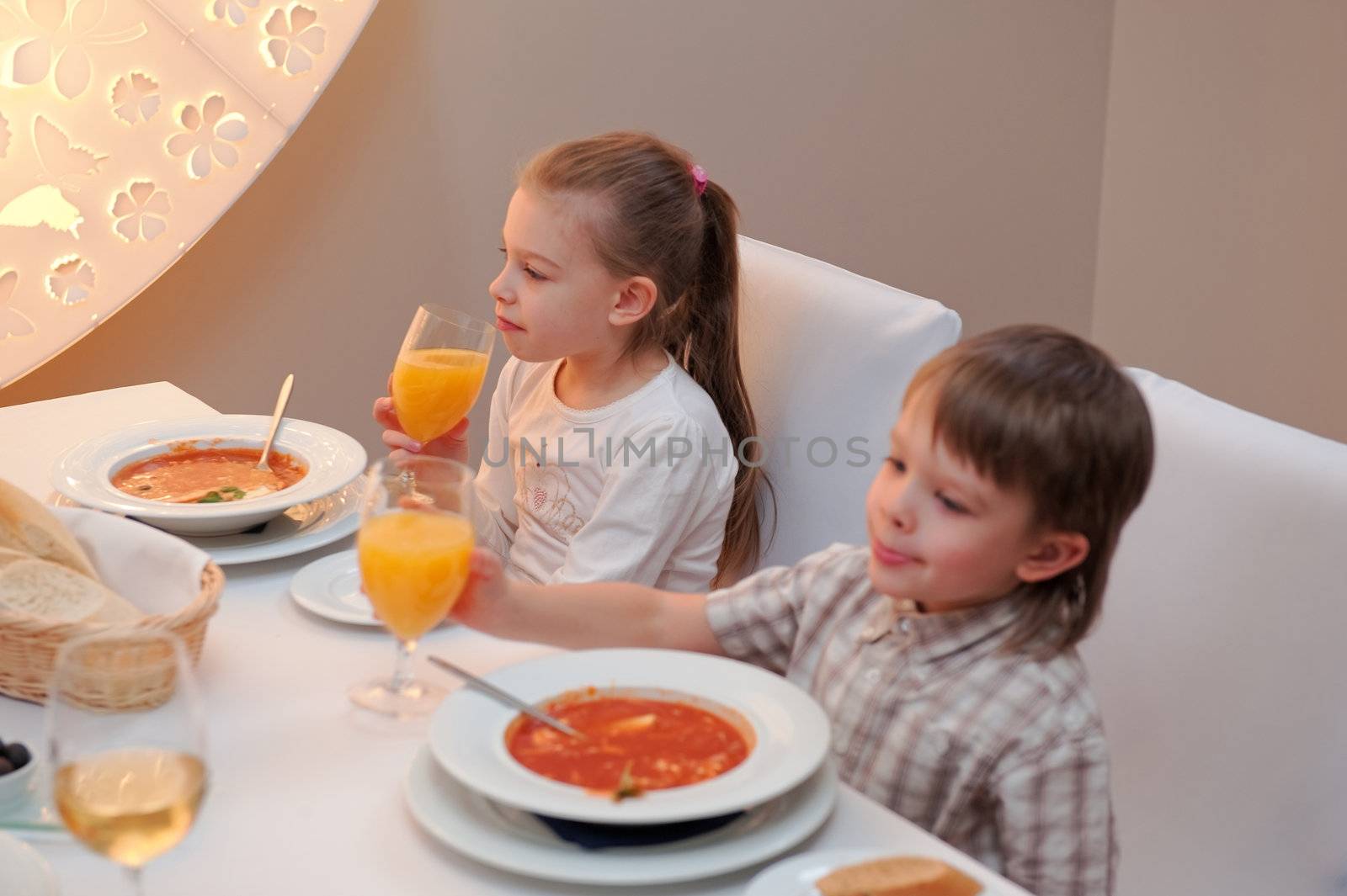 Sister and brother enjoying meal sitting at restaurant table. Girl in focus, boy out of focus.