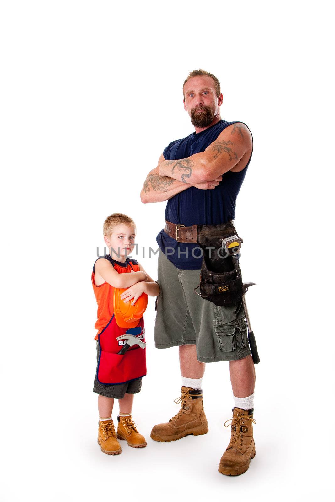 Caucasian middle aged father and cute young son ready to do a construction job. Man and boy wearing tool belt with hammer, shorts and boots, standing with arms crossed. Isolated.