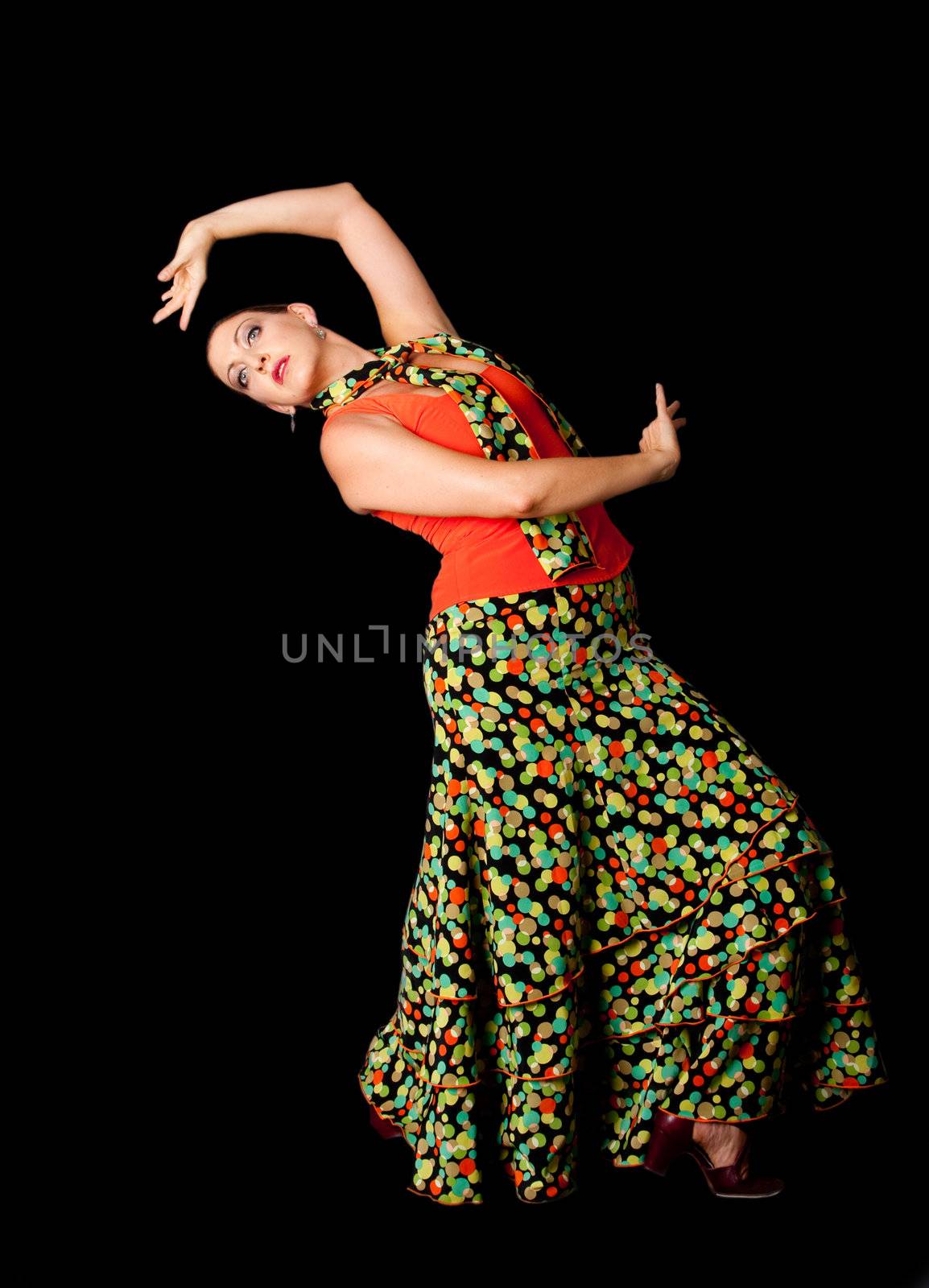 Beautiful modern Spanish Caucasian Flamenco and Paso Doble dancer wearing a colorful skirt with polka dots and orange shirt doing a line pose, isolated on black.