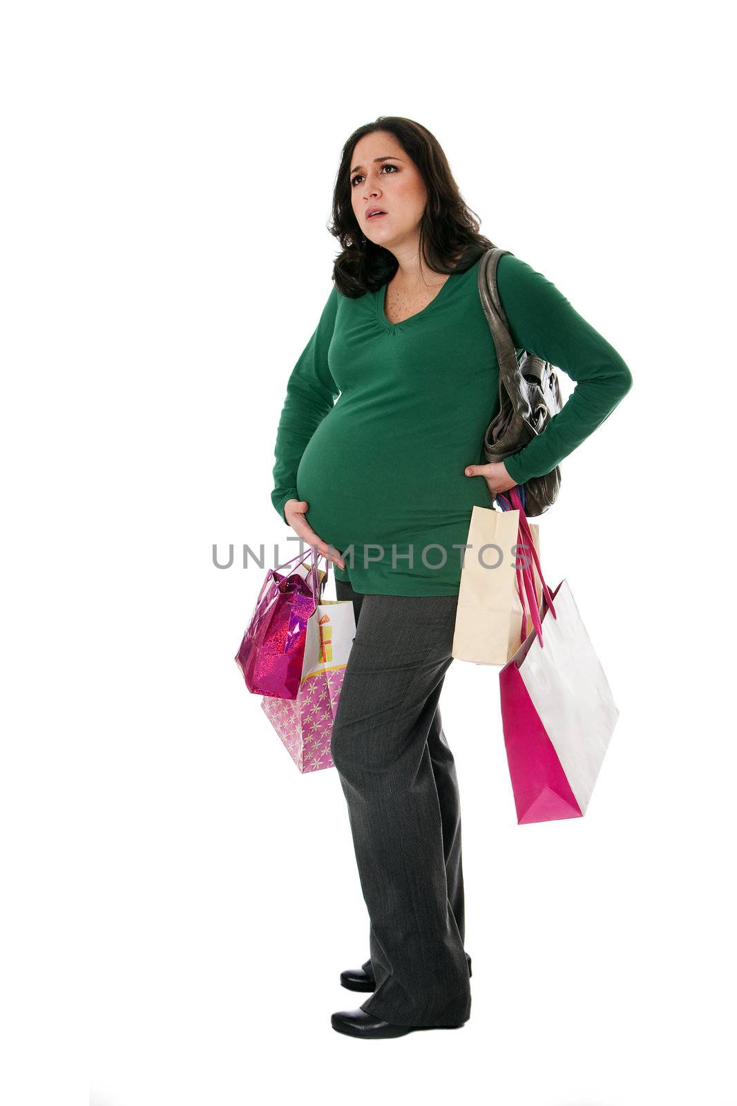 Beautiful Caucasian pregnant brunette woman holding shopping bags while standing expressing pain and holding belly as if her water broke, isolated