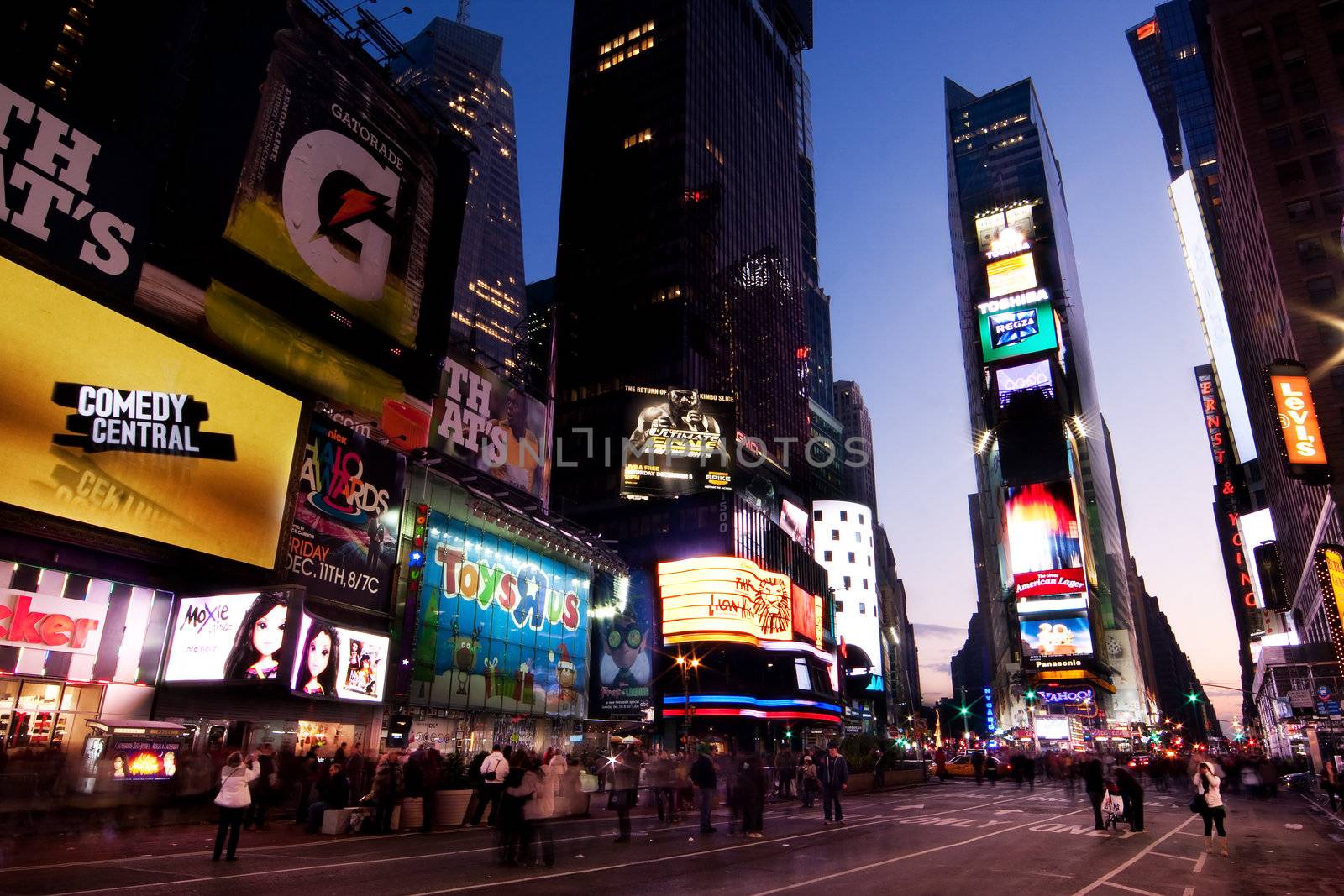 Night scene of Times Square in Manhattan (New York City) with all the lit up billboards and advertisements, and many tourists people walking by.