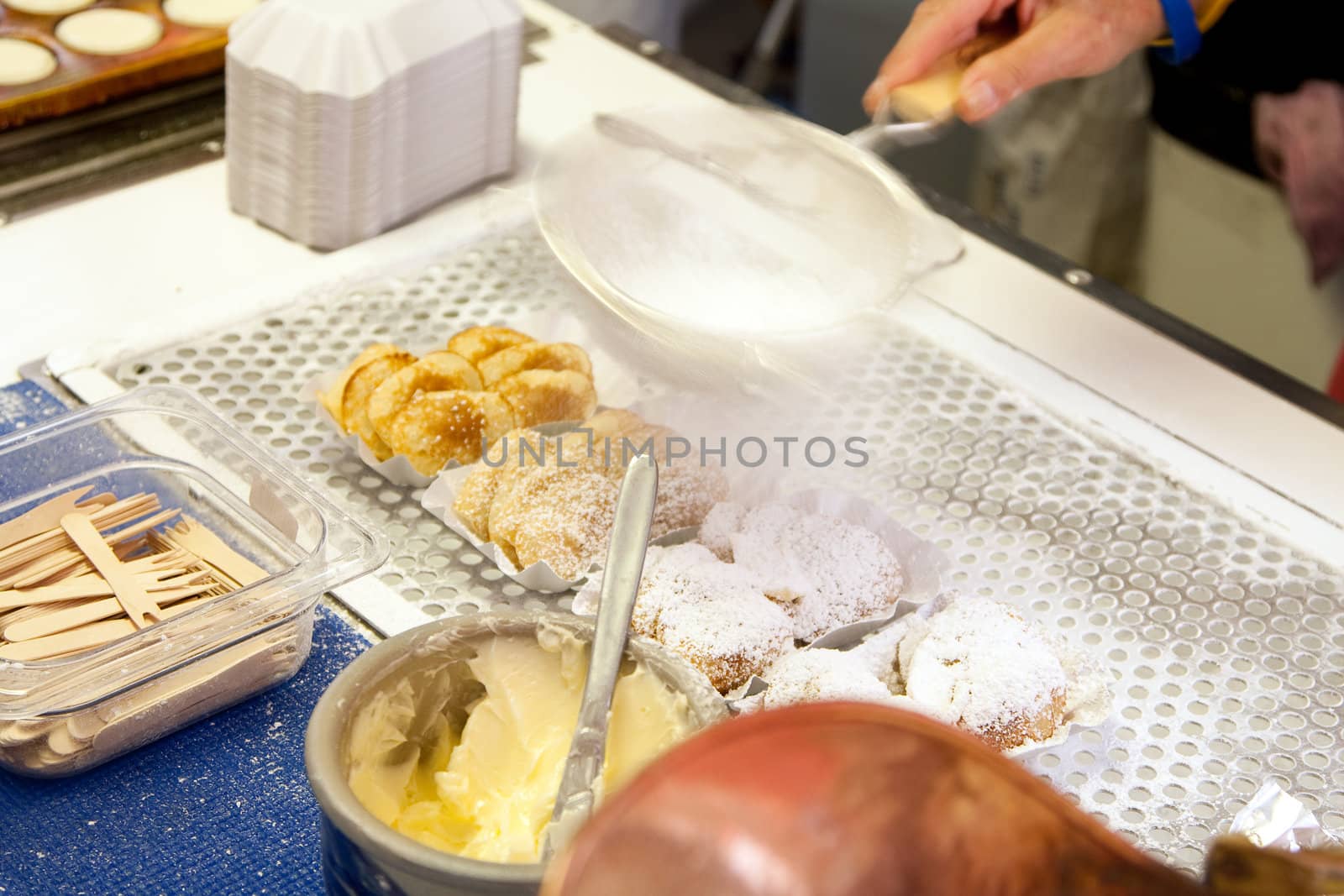 Delicious authentic Dutch food from The Netherlands called poffertjes, which are mini pancakes, being prepared for sale by adding butter and powdered confectioners sugar with a strainer.