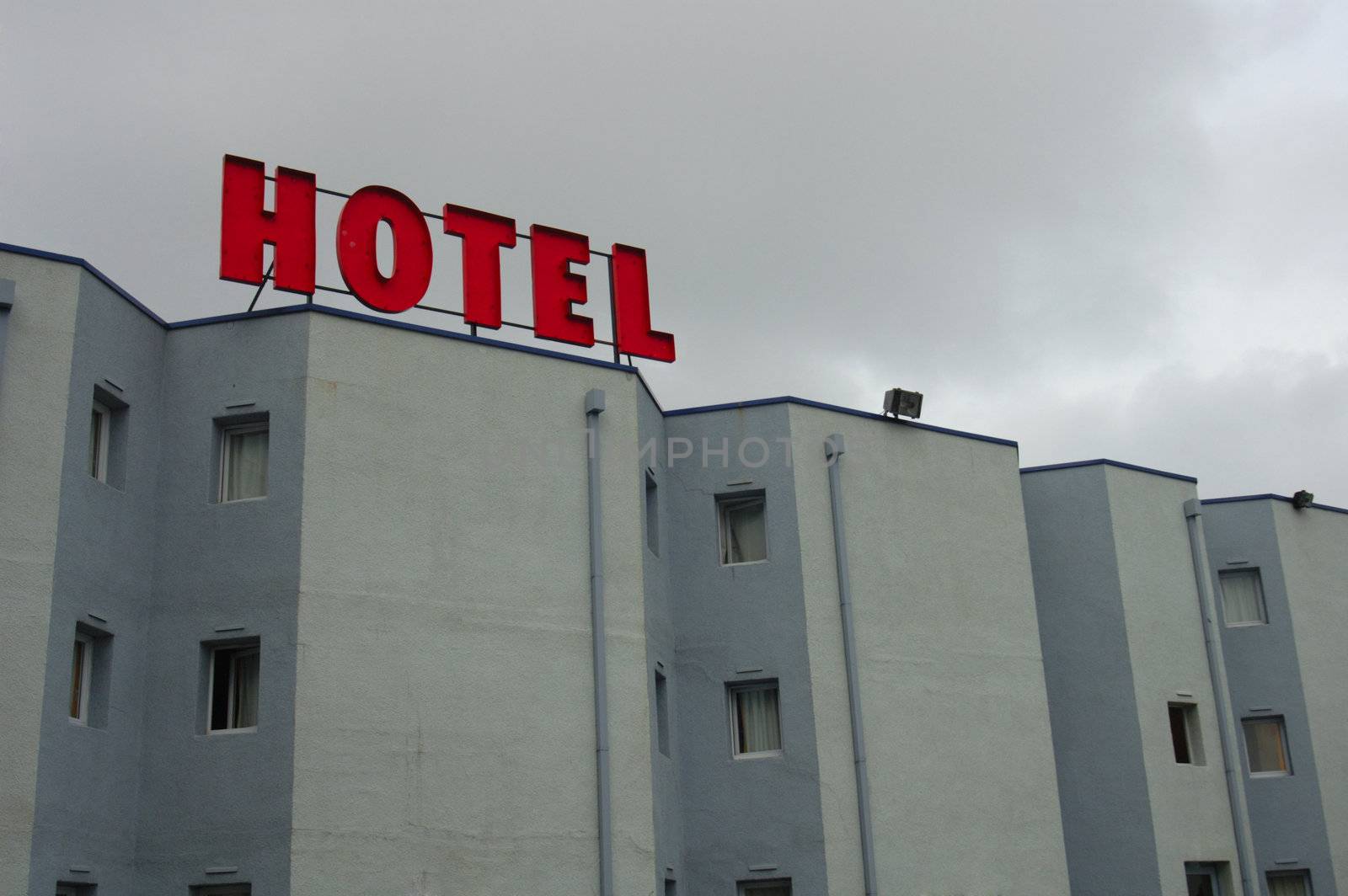 Grey walls, tiny windows, blocky architecture, all under a grey sky. The only bright thing about this hotel is its sign. Space for text in the sky.