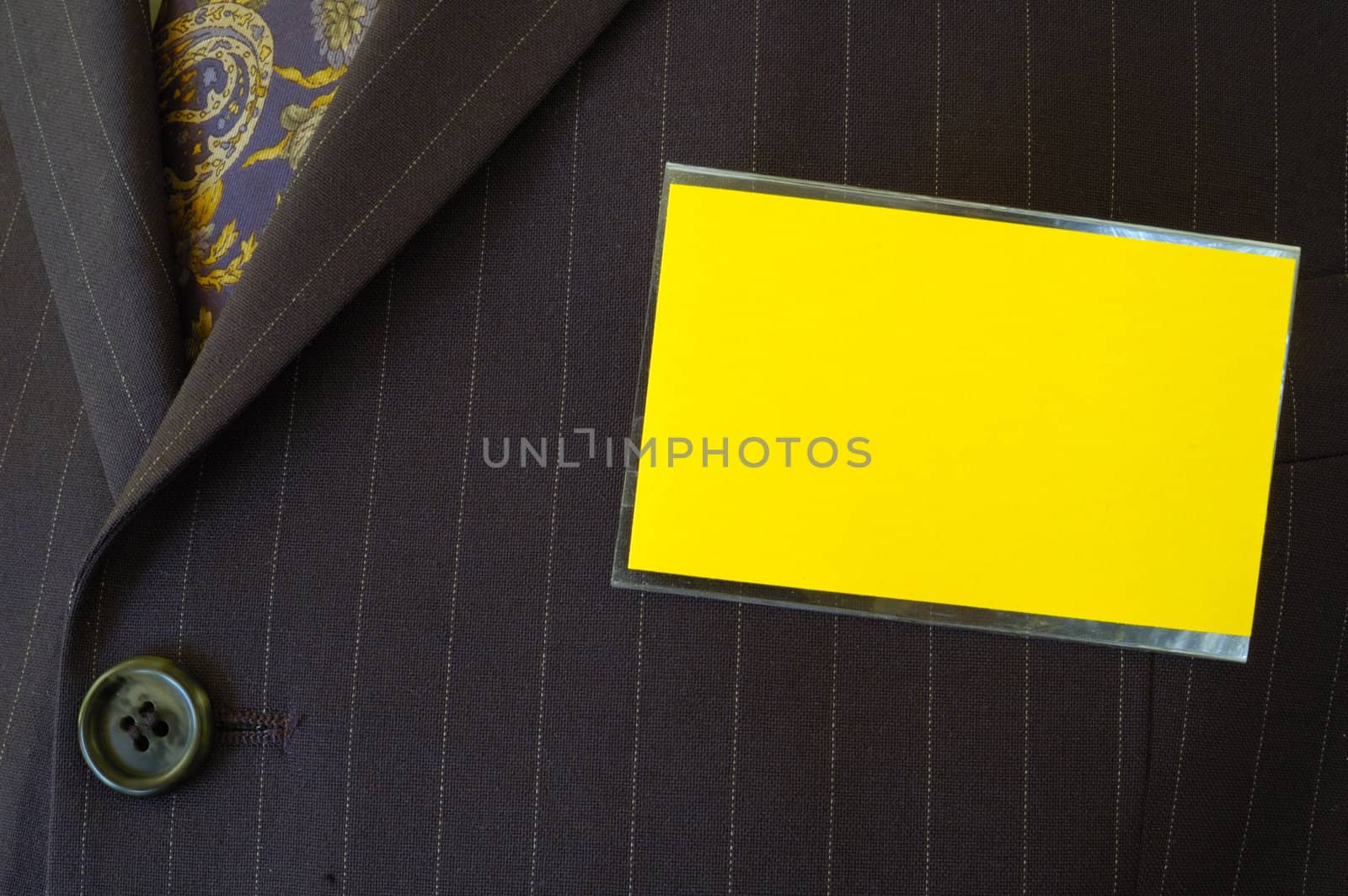 Close-up of a blank yellow name-tag on a businessman's pin-striped suit. Space for text on the tag.