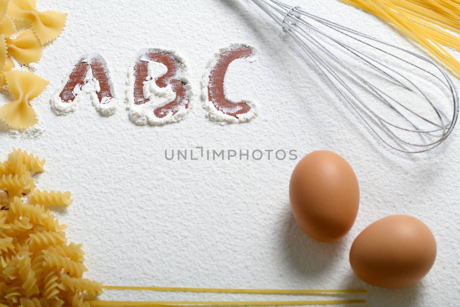 Uncooked macaroni, whisk and eggs on wheat flour, background