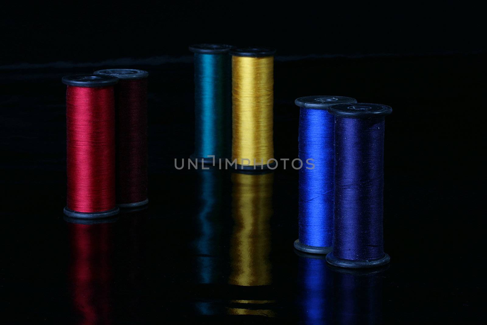 Colour threads of different colours for sewing on industrial coils, the picture is made by hectare a black reflecting background.