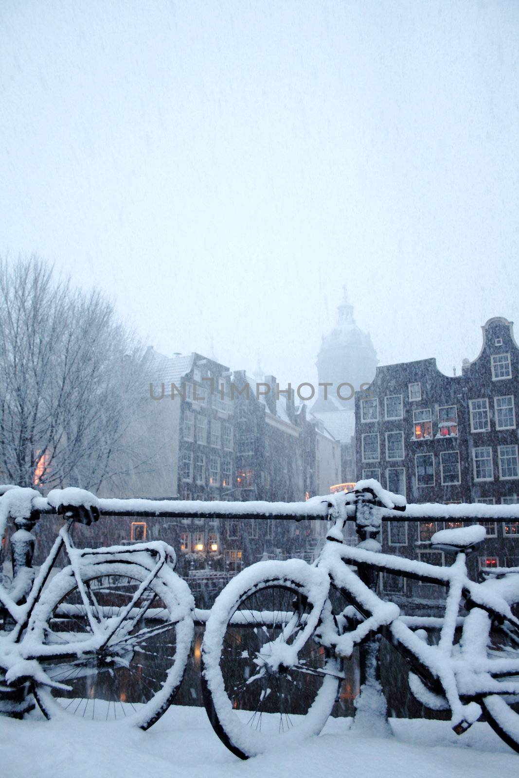 A bicycle stands under heavy snowstorm on background with buildings in Amsterdam