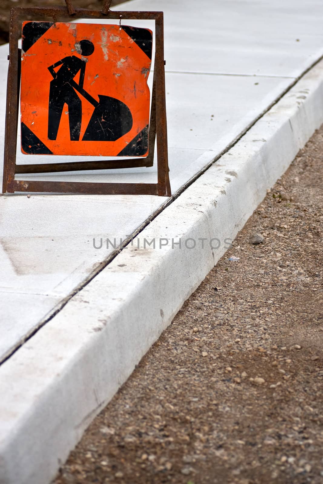 Brand new sidewalk with focus on an orange construction worker sign.