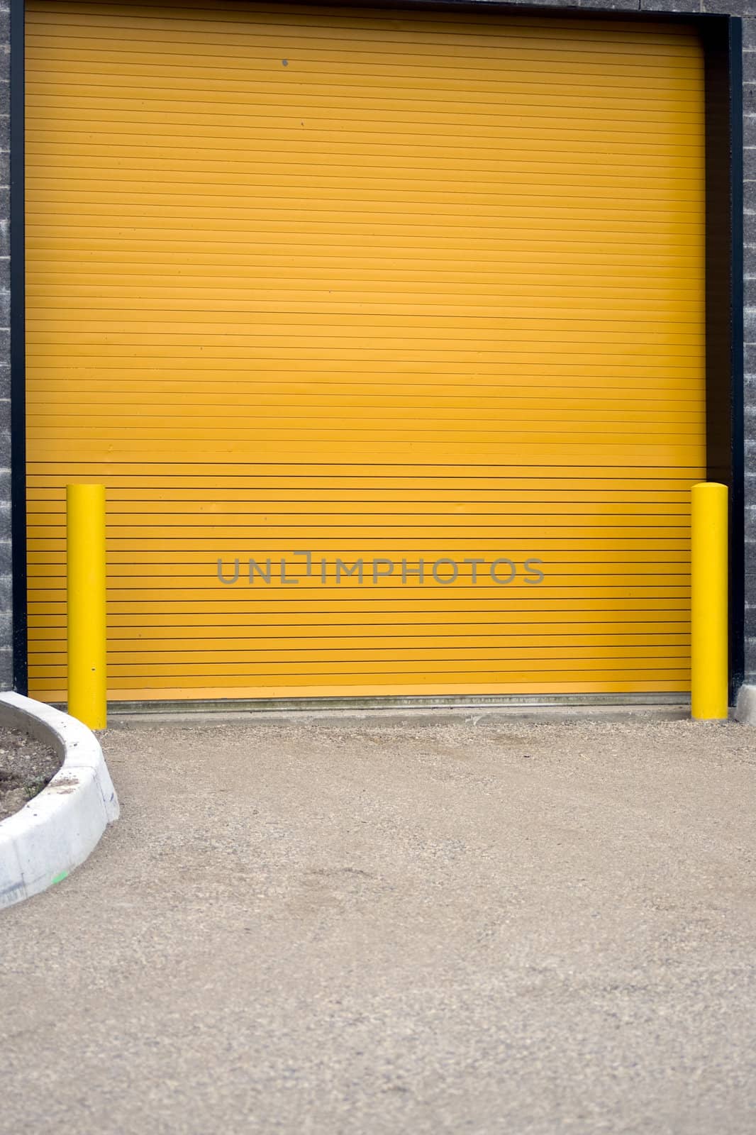 A colorful industrial garage door, with yellow barriers on either side.  This door is actually on the side of a hockey rink, for Zamboni's to exit the rink and dump the snow that they scraped from the ice.