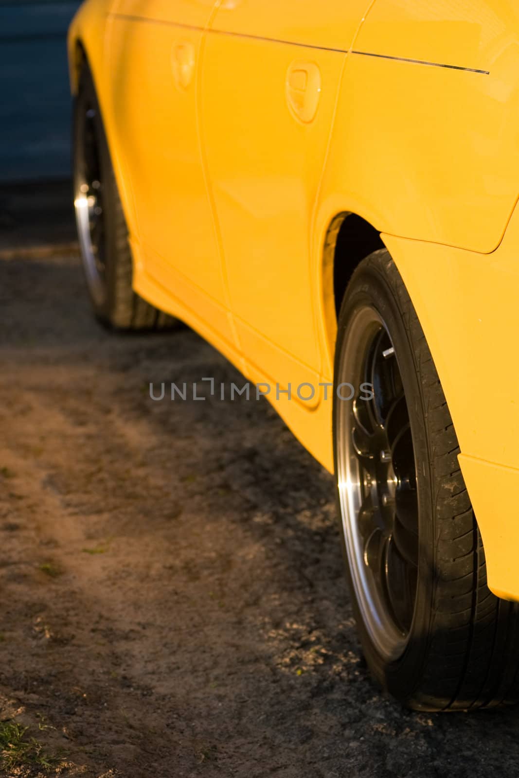 A closeup of the side of a yellow car, with custom black rims.