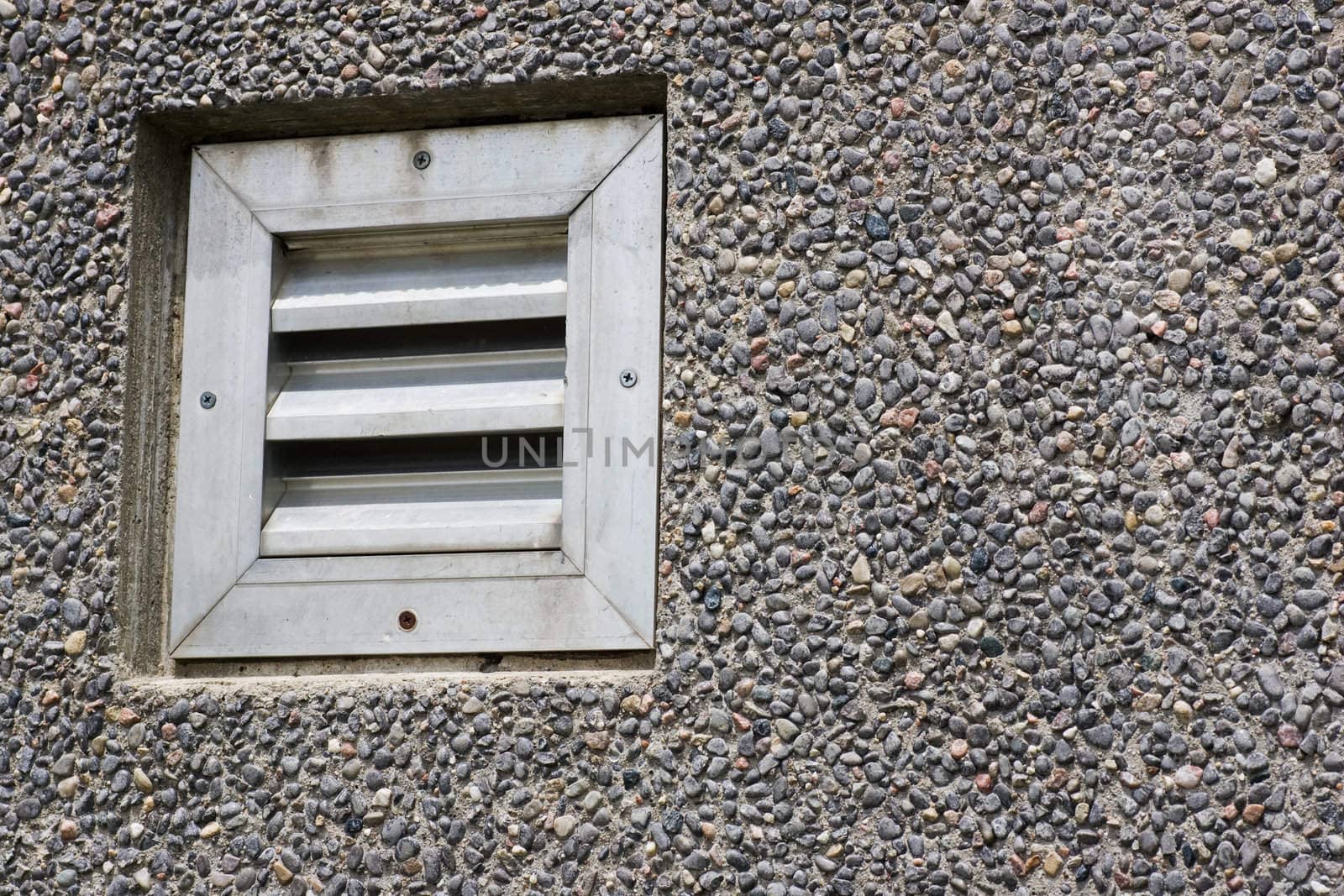 A louvered vent on a pebble textured wall.