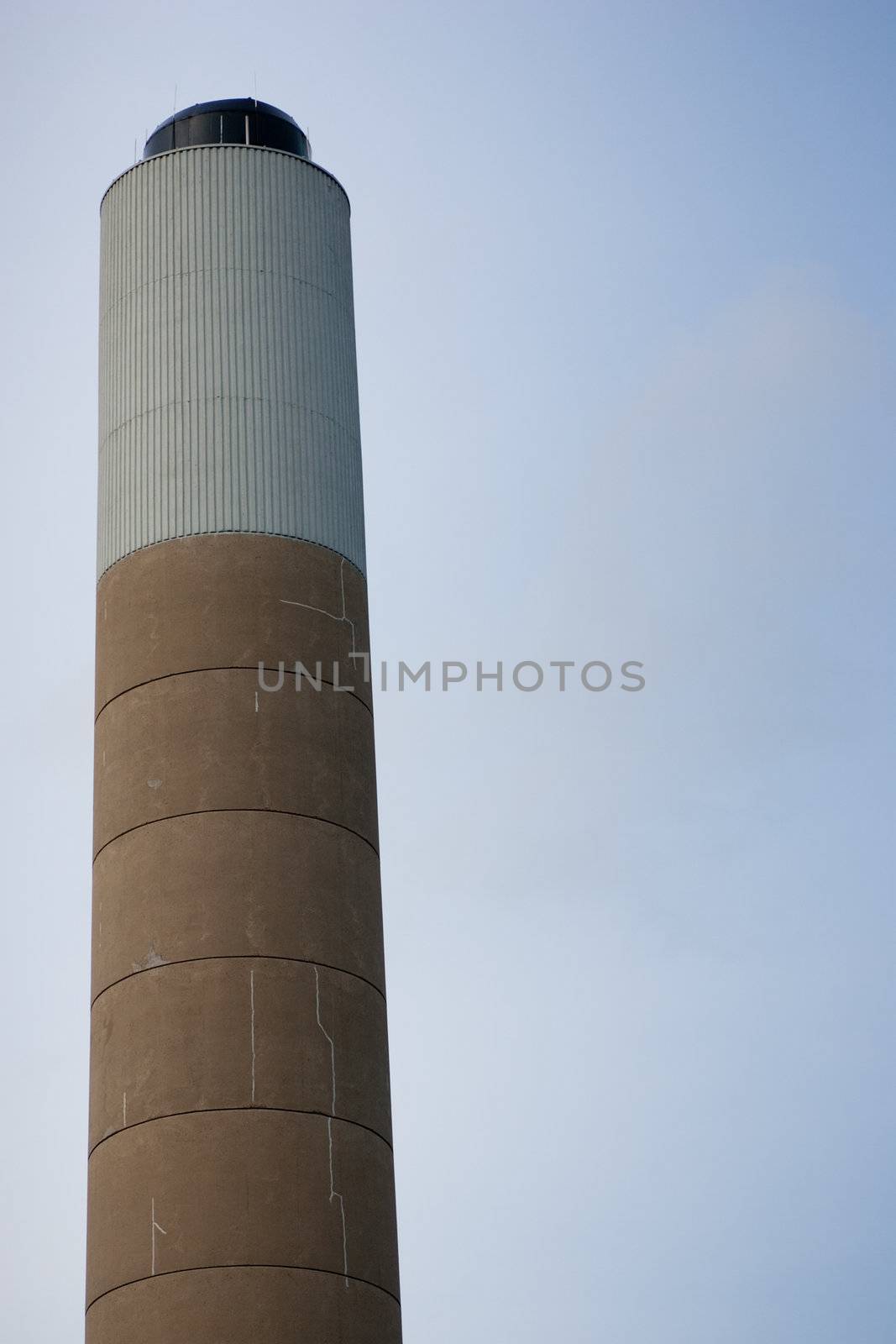 Closeup of the top of a smoke stack, with signs of cracks, isolated against a clear sky.