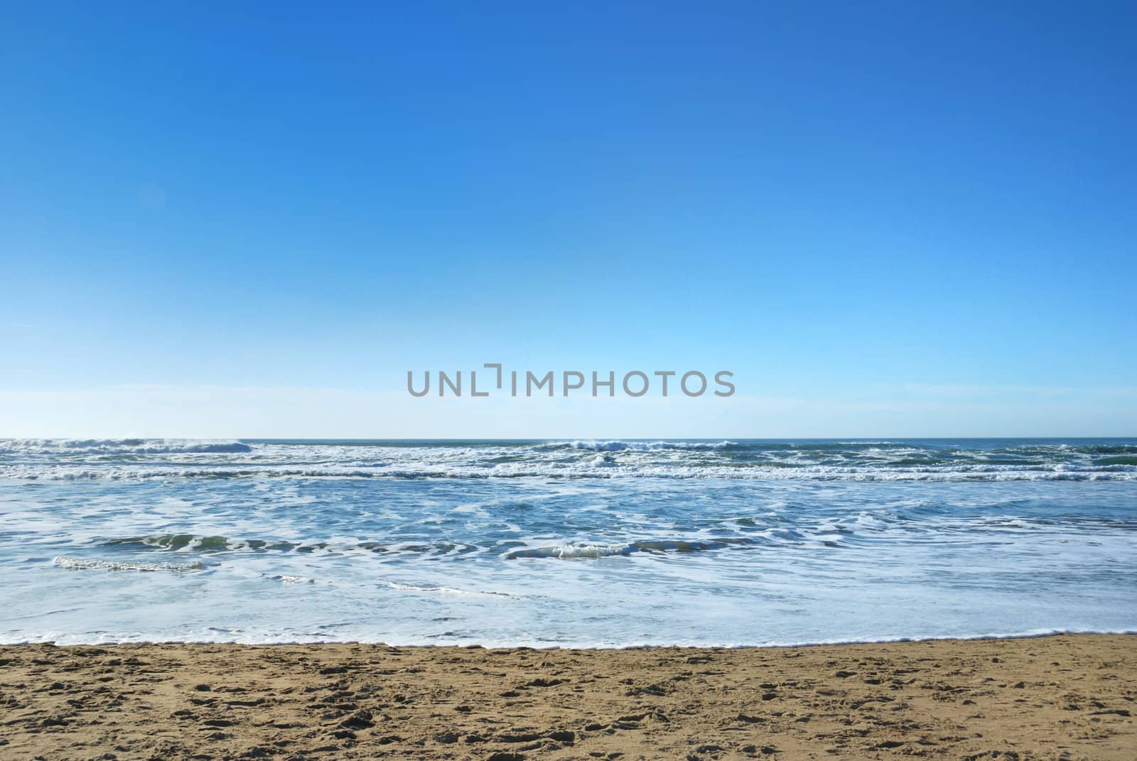 Ocean Beach in San Francisco California with waves coming to the sand and blue sky background.