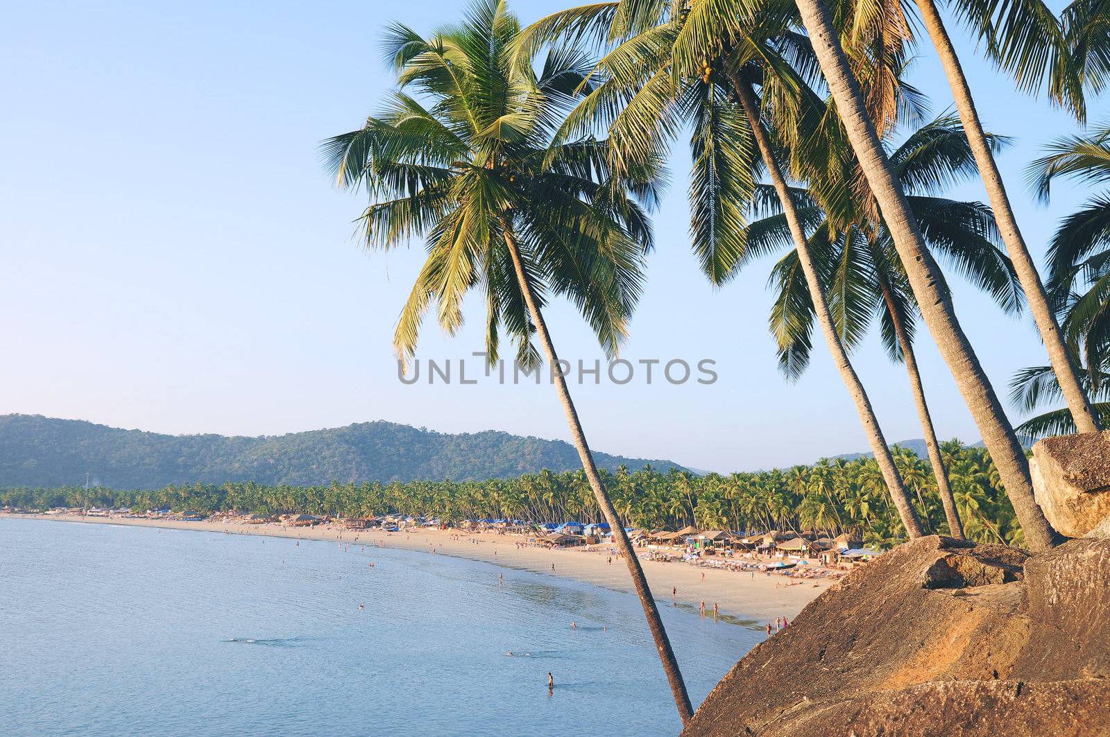 Palm trees with beautiful seascape on background with mountains, bay, sand beach and shacks.