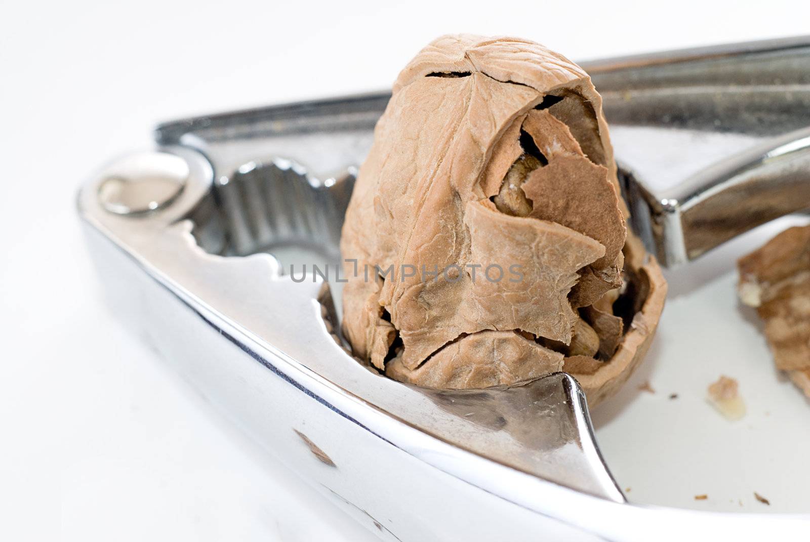 A partially cracked walnut being cracked by a nutcracker, shot on white