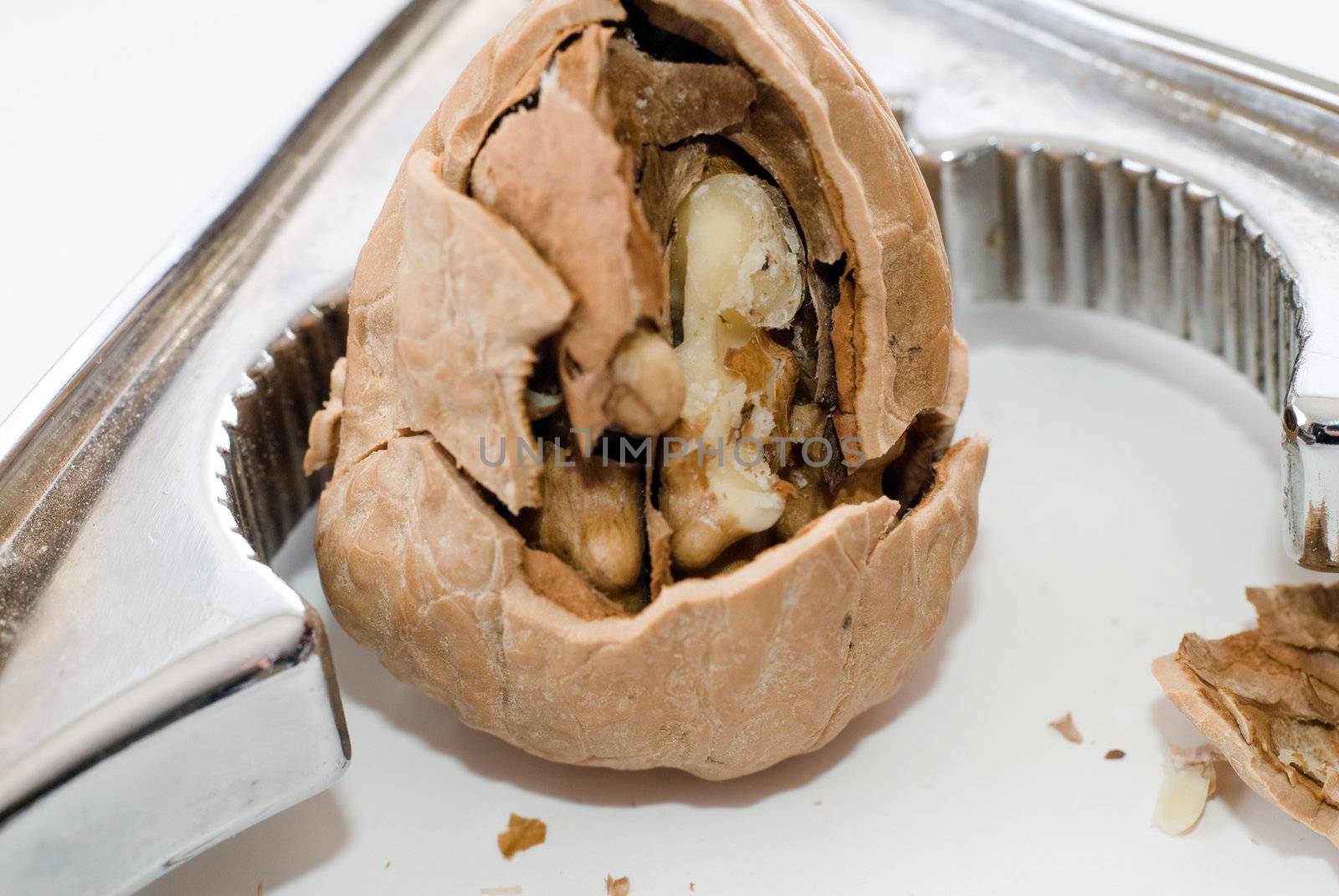 Closeup of a cracked walnut with a silver nutcracker, shot on a white background