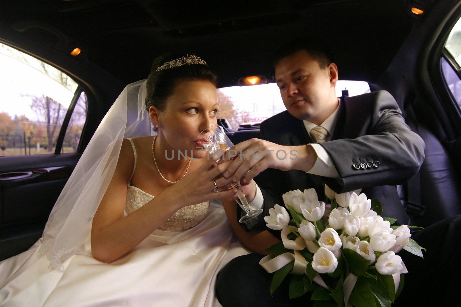 The bride with the groom drinks champagne in the automobile