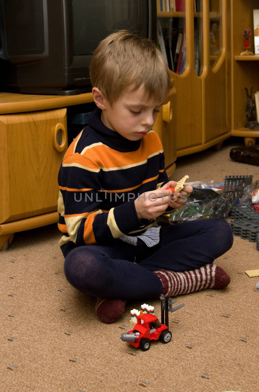 The boy sits on the floor and plays in the meccano.