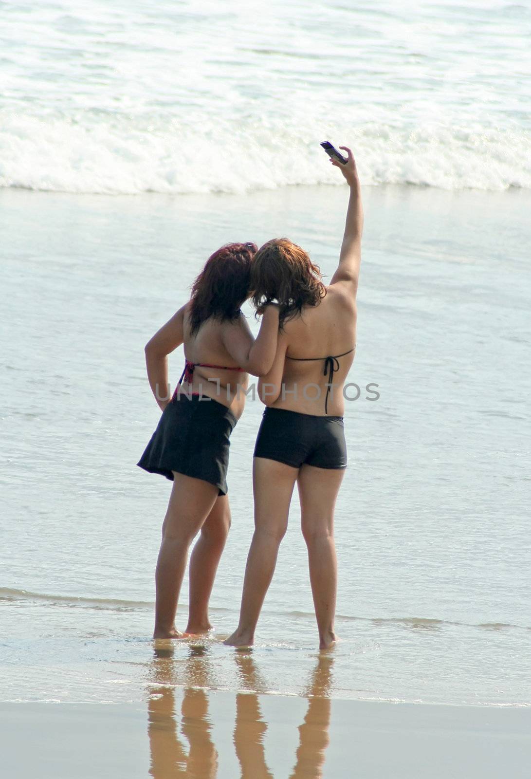 two girls on beach taking picture with camera phone