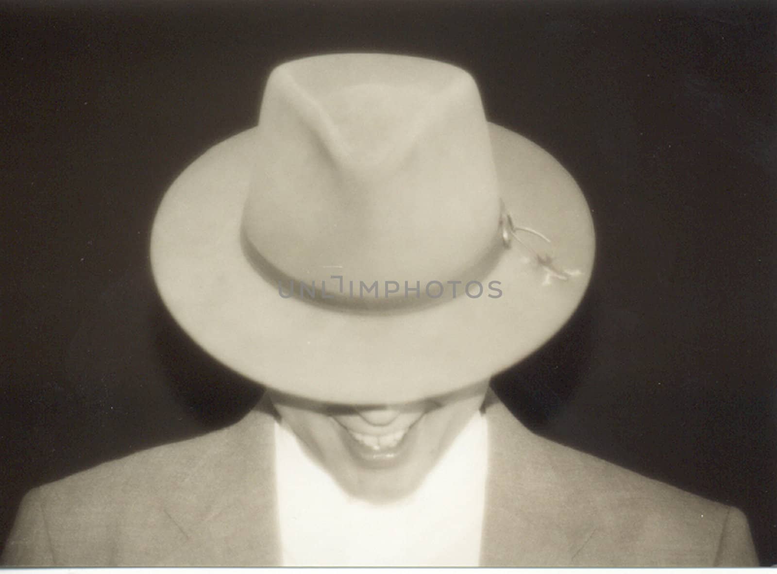 monotone portrait of mystery man hiding behind hat while smiling
