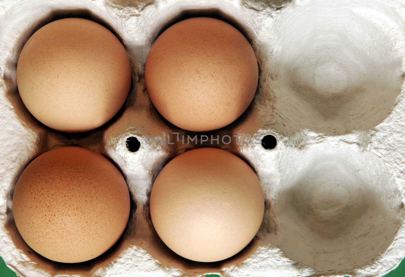 Four Brown Eggs In A Grey Cardboard Box On Green Background