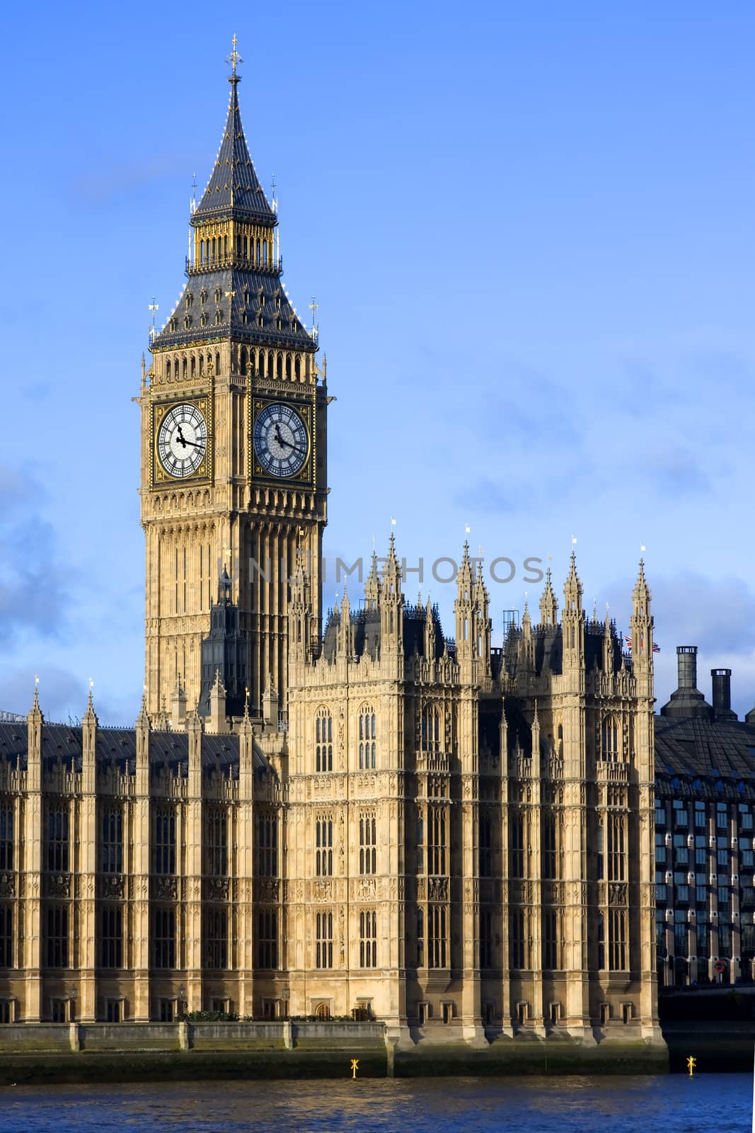 An evening shot of the Palace of Westminster, Big Ben and the River Thames, London England against a blue sky