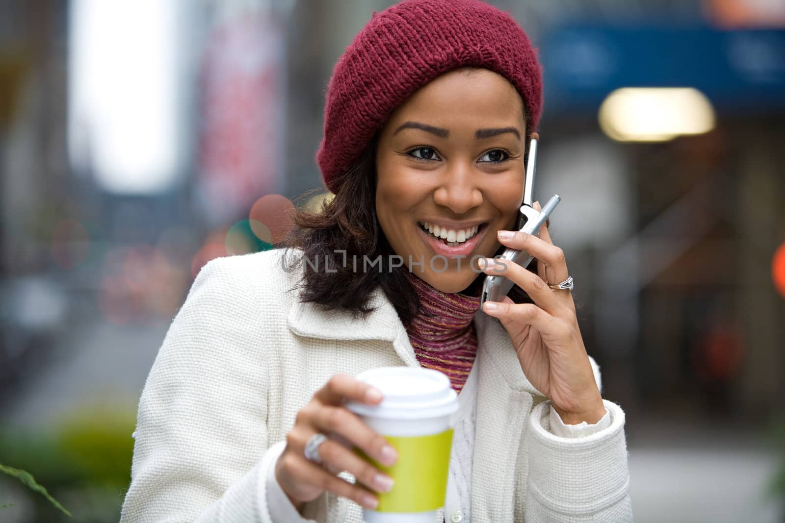 A modern business woman in the city talks on her cell phone while enjoying a cup of coffee.