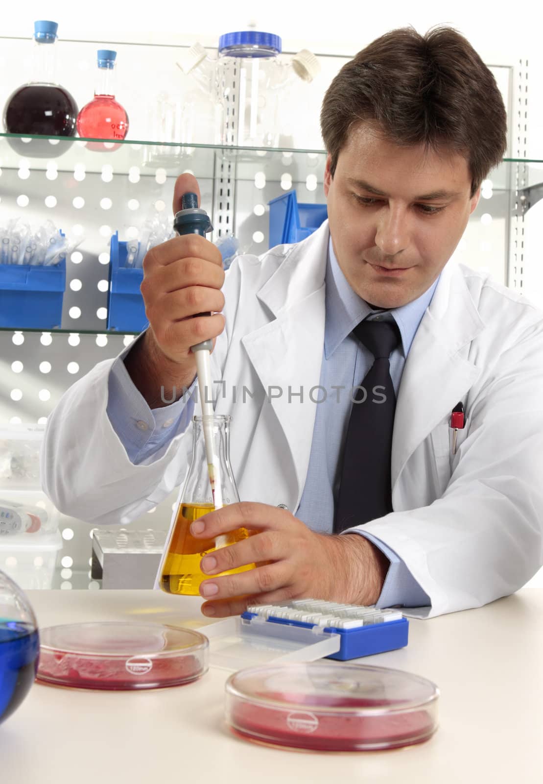 A male scientist, pharmacist or researcher using a pipette to take a sample fluid from erlenmeyer flask in a laboratory.