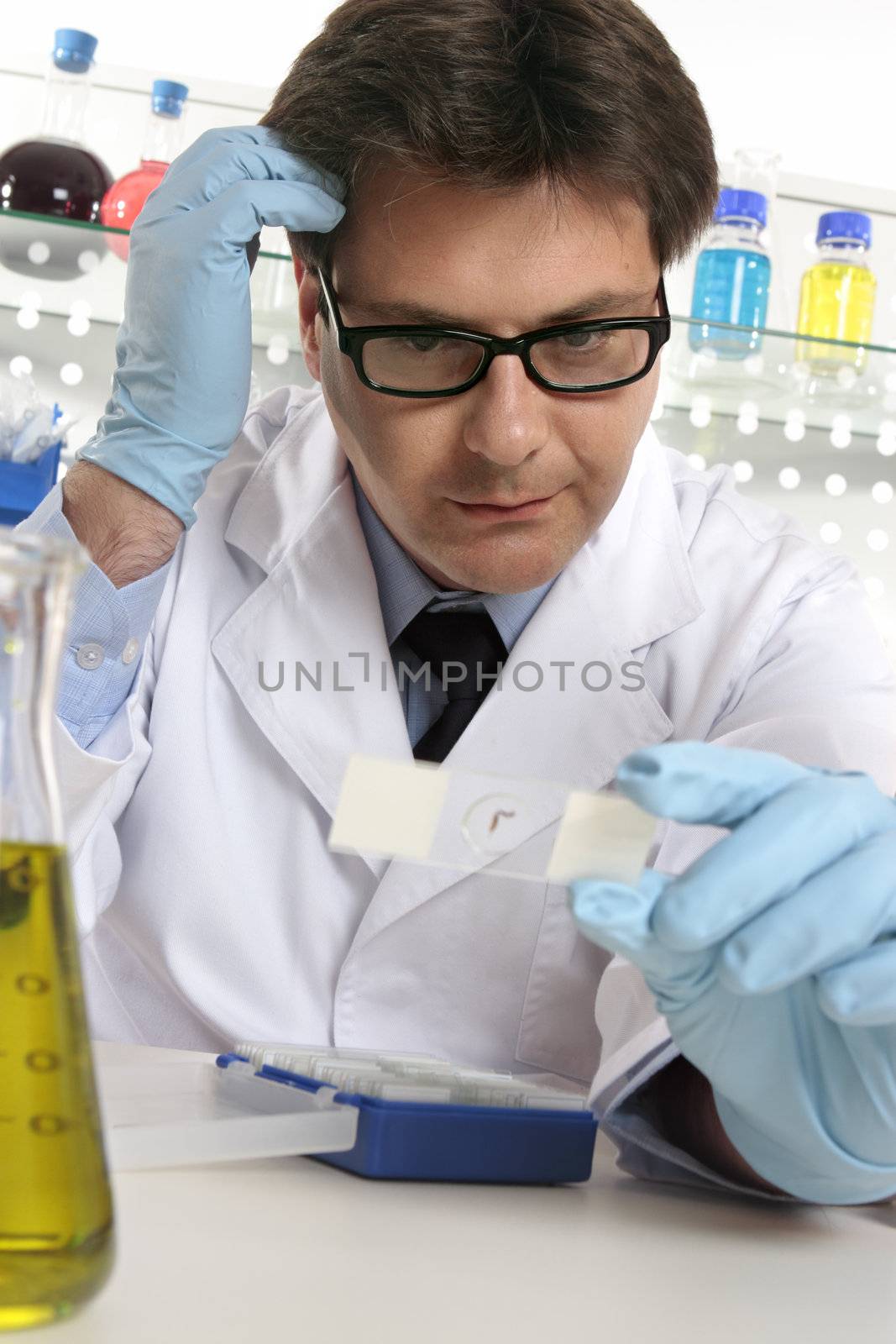 A scientist scratches his head whilst examining a microscope slide.