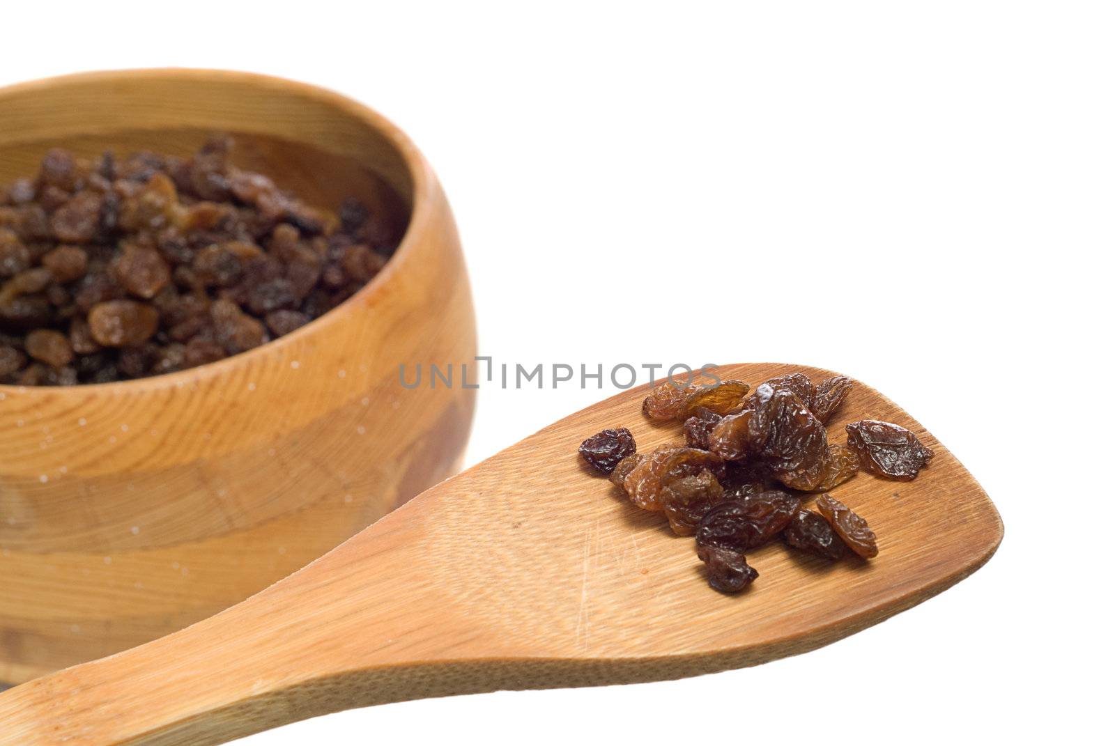 A small cluster of sundried raisins being displayed on a wooden spatula with more in a bowl OOF in the background