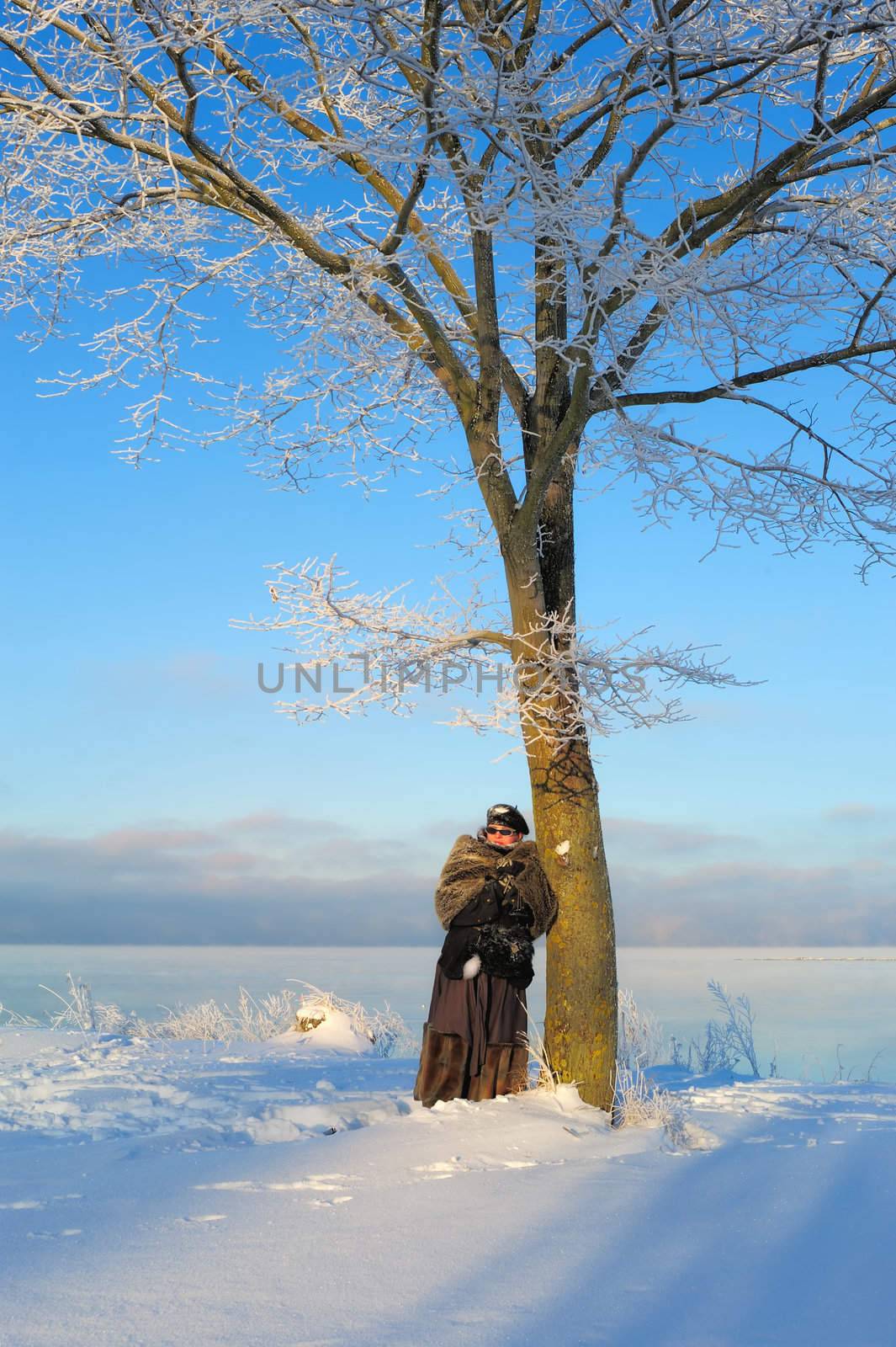 Woman stands near a frozen tree on the shore