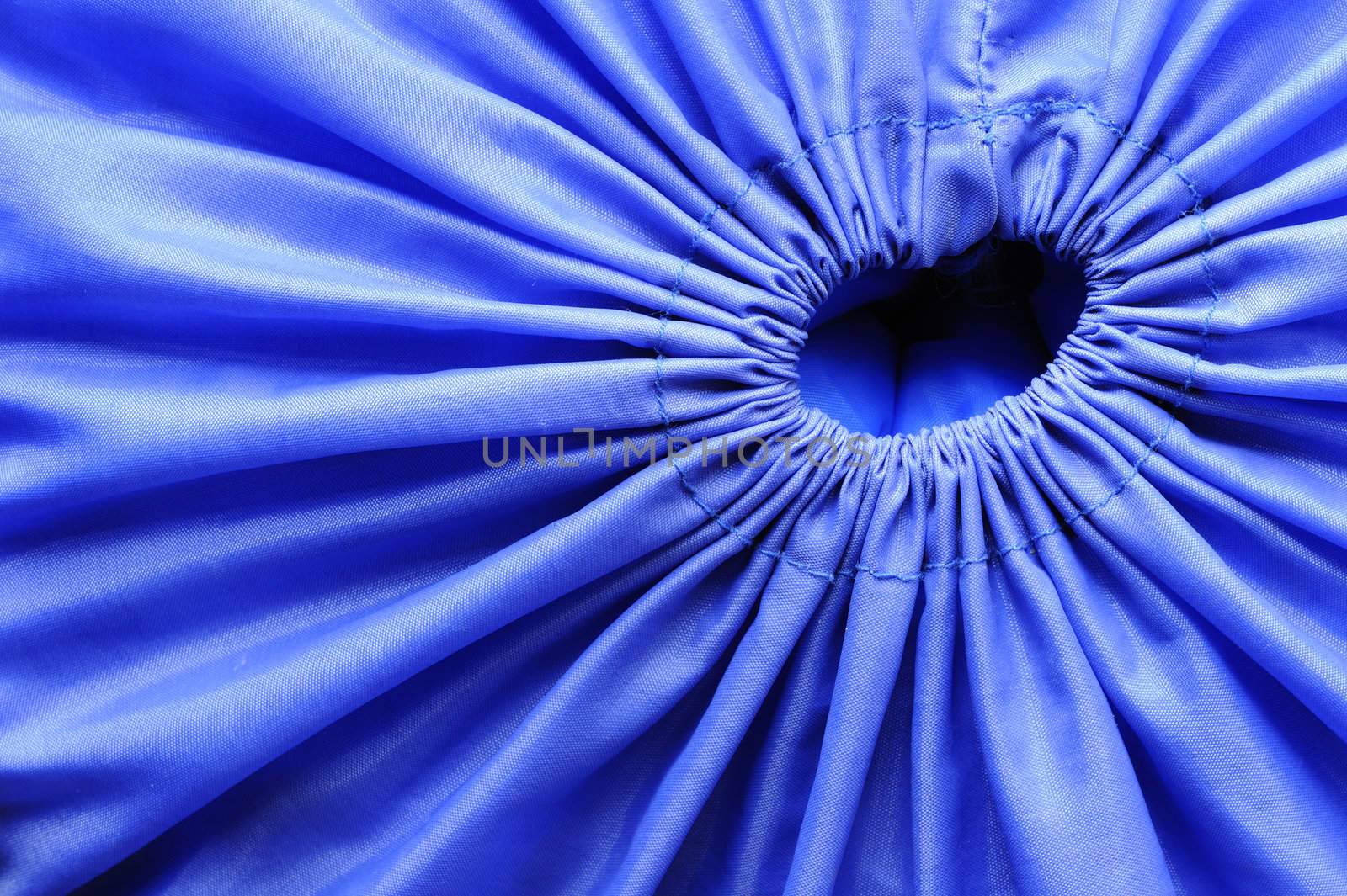Macro image of the opening of a blue fabric bag, drawn tight closed by a drawstring.