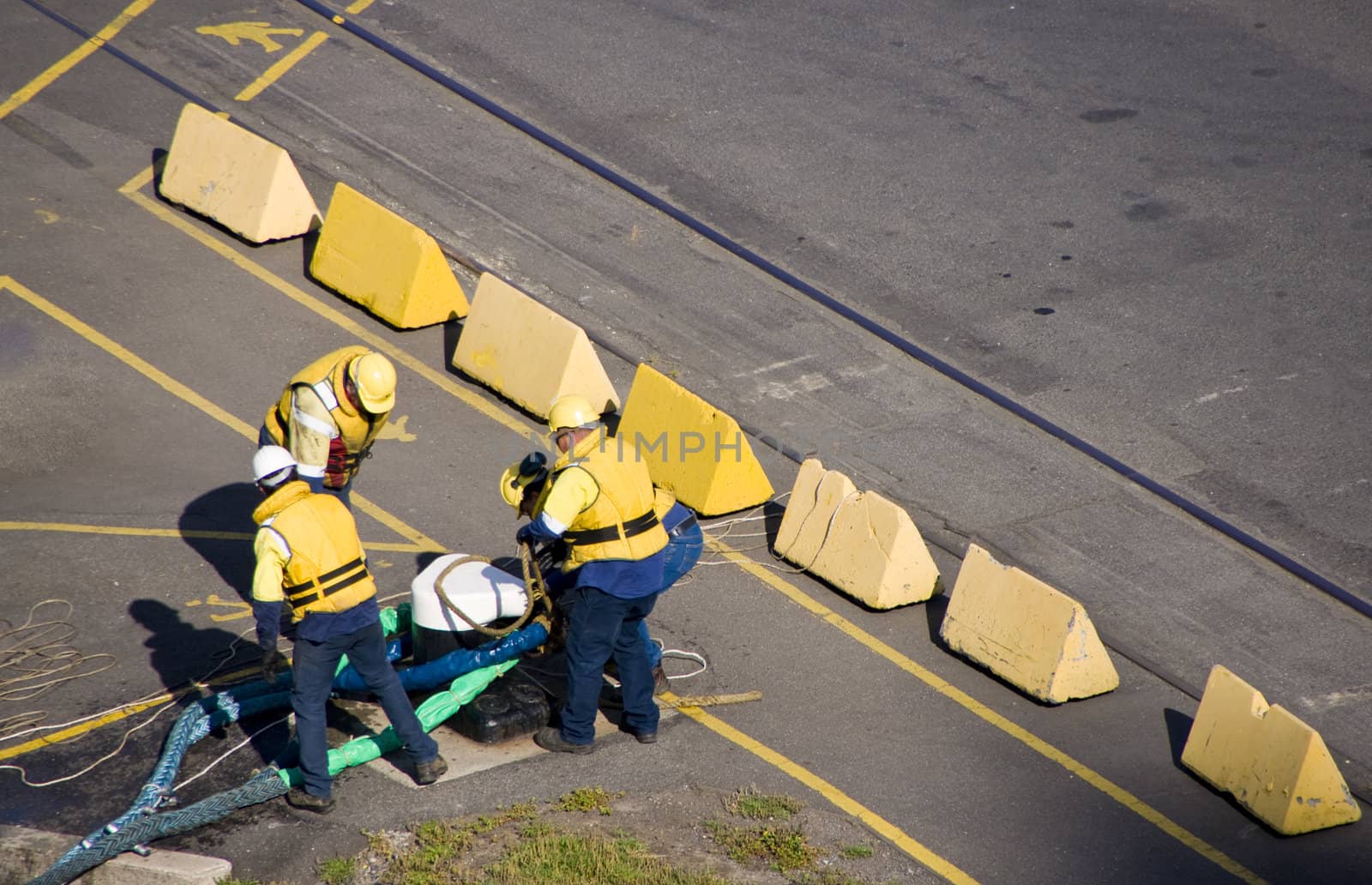 Four helmet longshoremen carry heave cable to moor the ship in port.