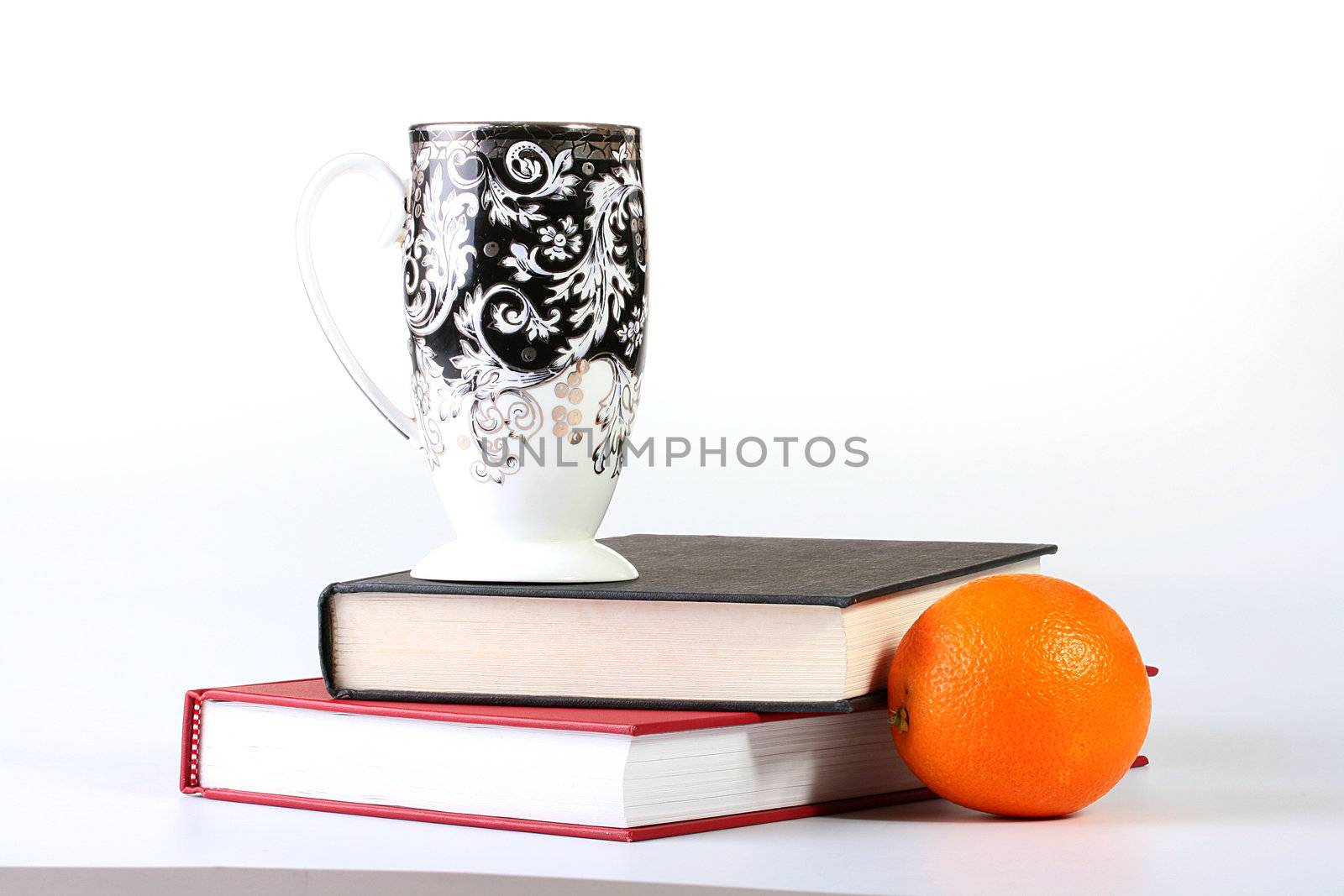 Two books with a high cup for tea and an orange.