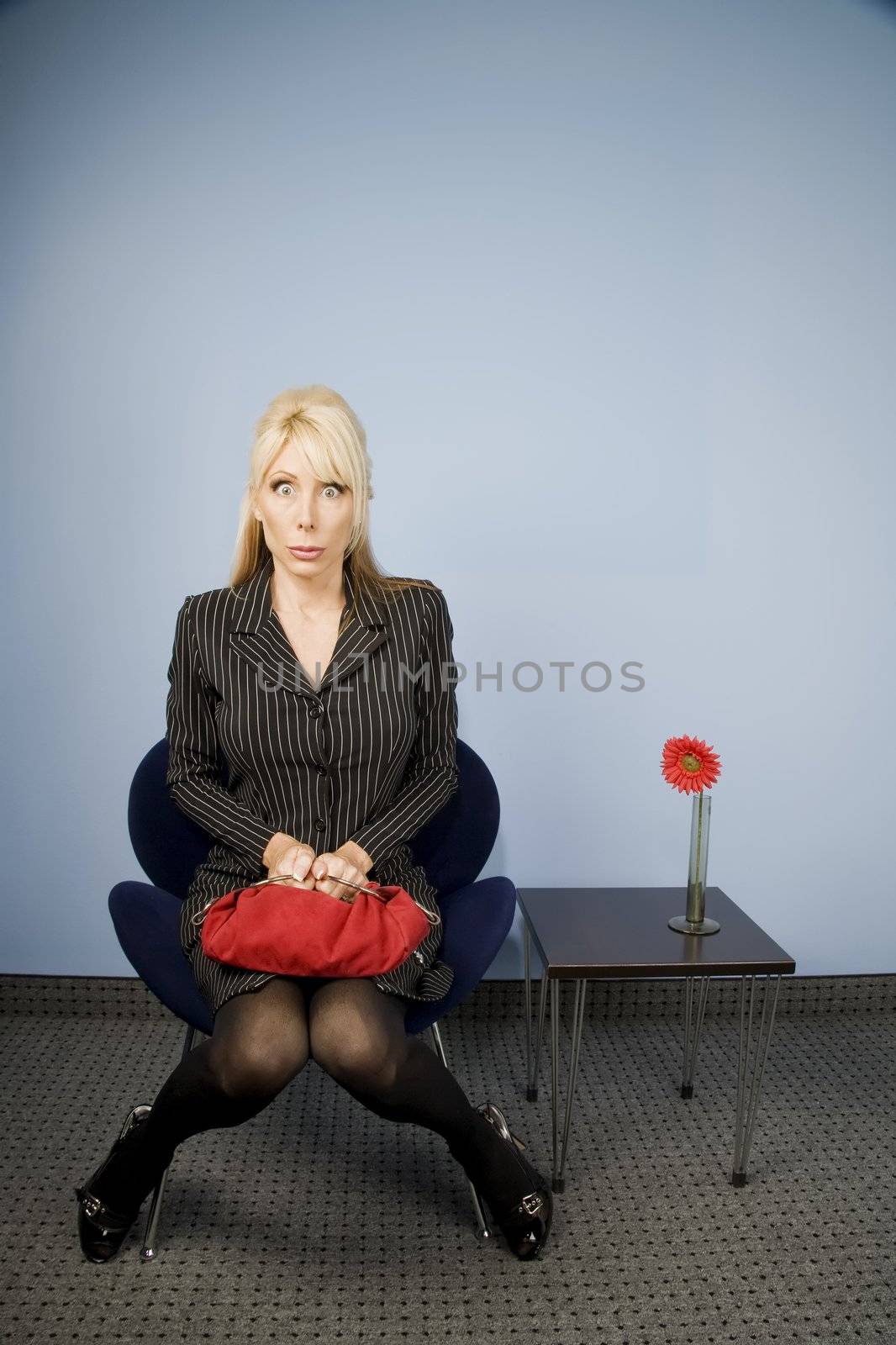 Apprehensive woman sitting waiting in an office chair  by Creatista