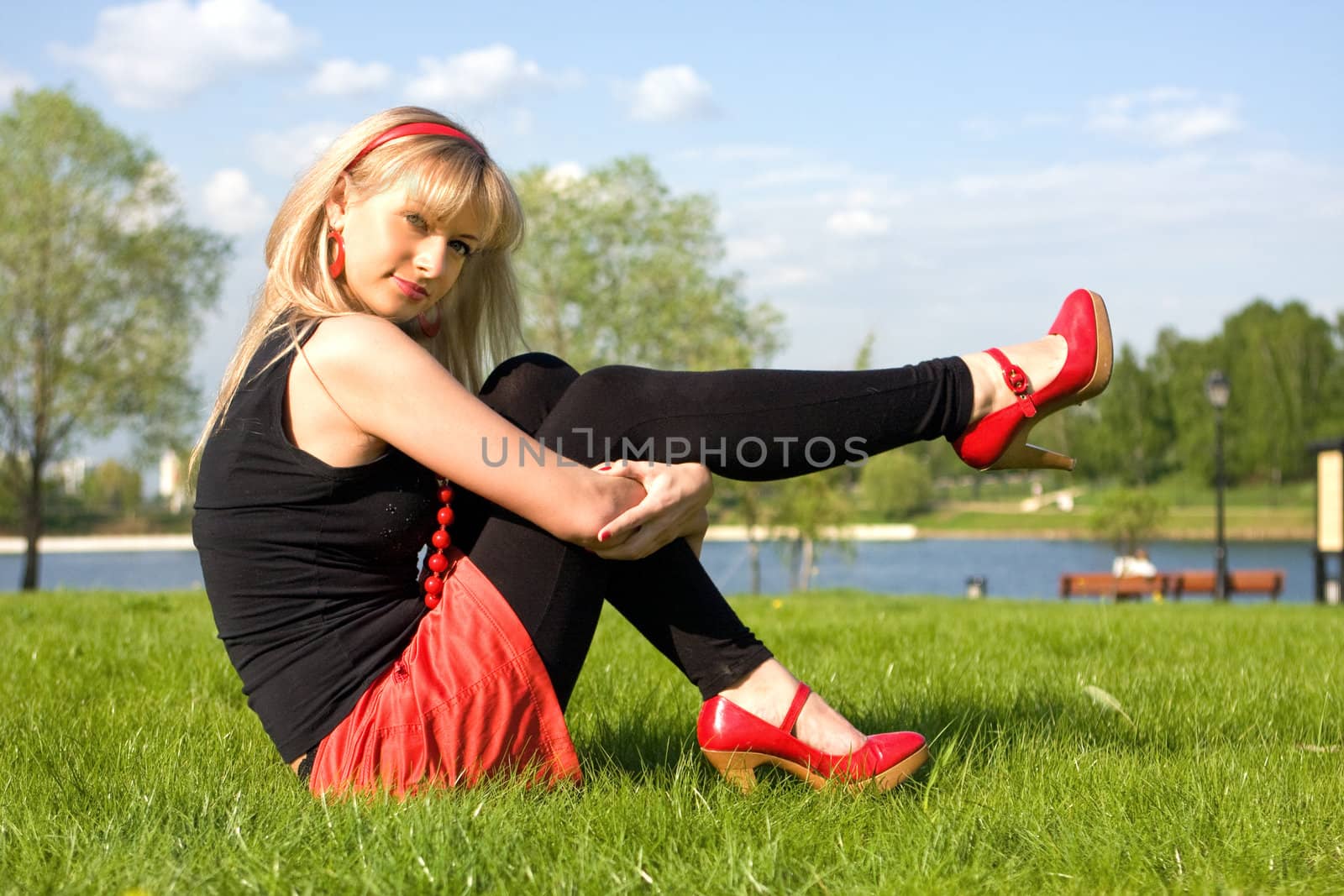 The girl sits on a grass on the bank of the river