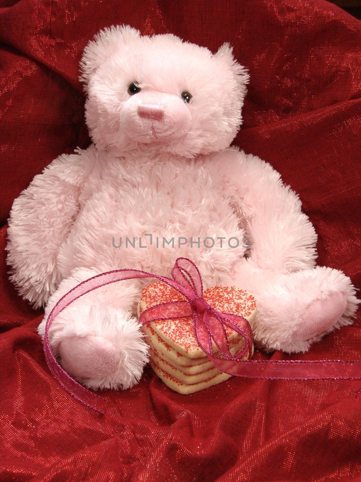 Pink Valentine bear with heart shaped cookies stacked and tied with ribbon. Red fabric background.