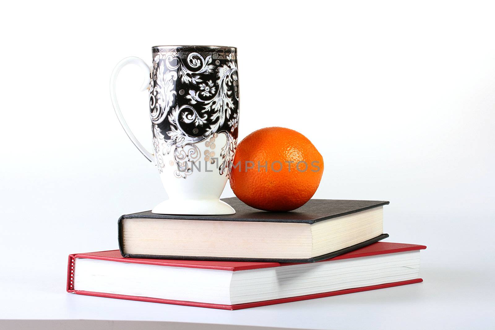 Two books with a high cup for tea and an orange.