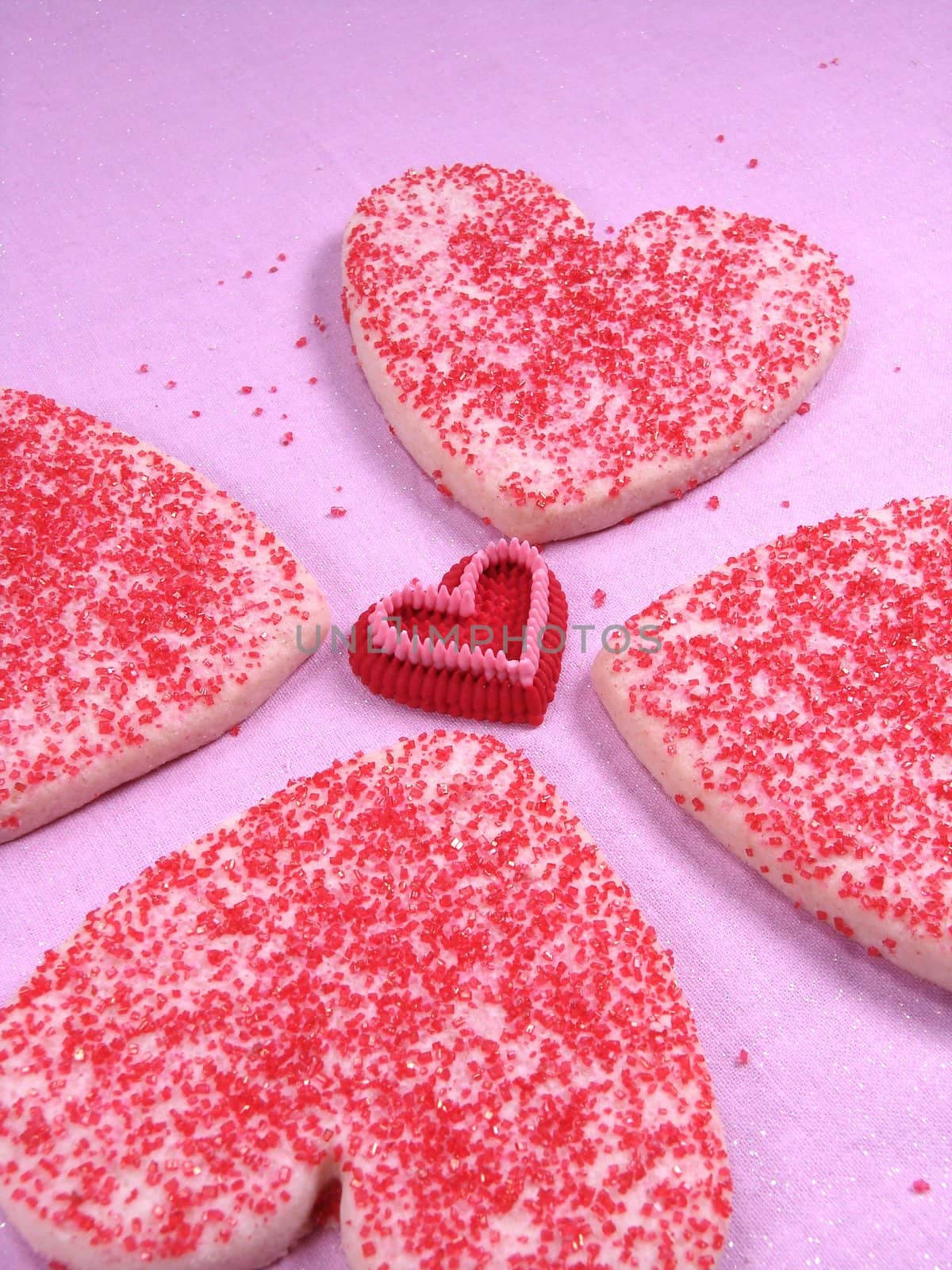 Simple heart sugar cookies sprinkled with red sugar. Cookies are placed on pink cloth.