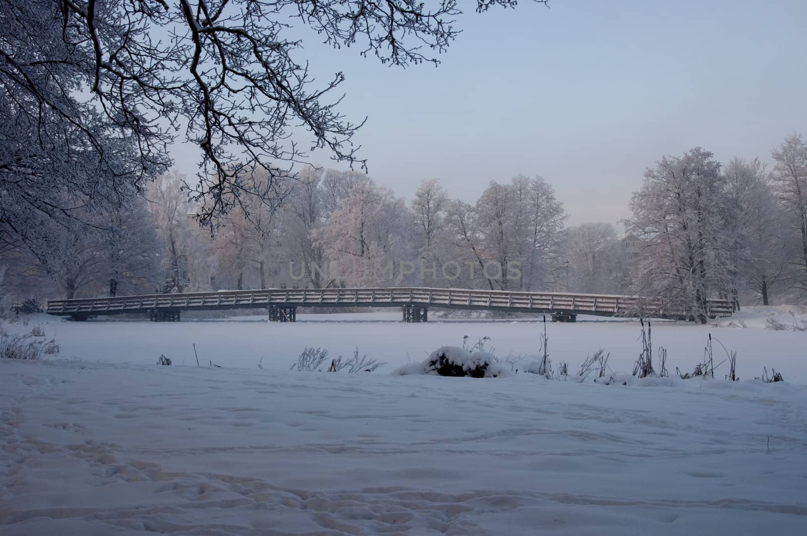 A wooden bridge over a frozen river a cold winter day.