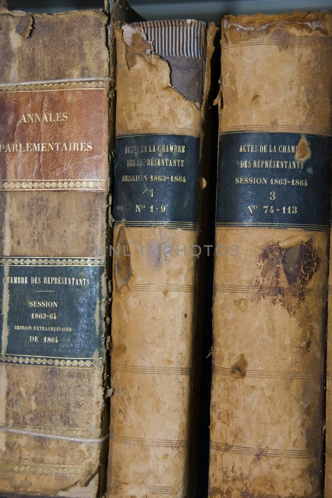 3 very old antique books, partly damaged by time, standing against neutral wall. Archives hold historical records of olden times.  These records are printed or written on, what are now very old papers, and kept in temperature-controlled rooms on racks. Consultation is only by permission and must be done in a controlled environment. The fragility of the papers demands a gentle handling. 