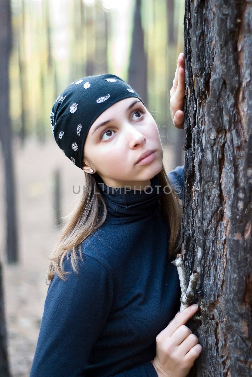 dreaming beautiful girl with bandana in the woods leaning against the trunk of a pine tree