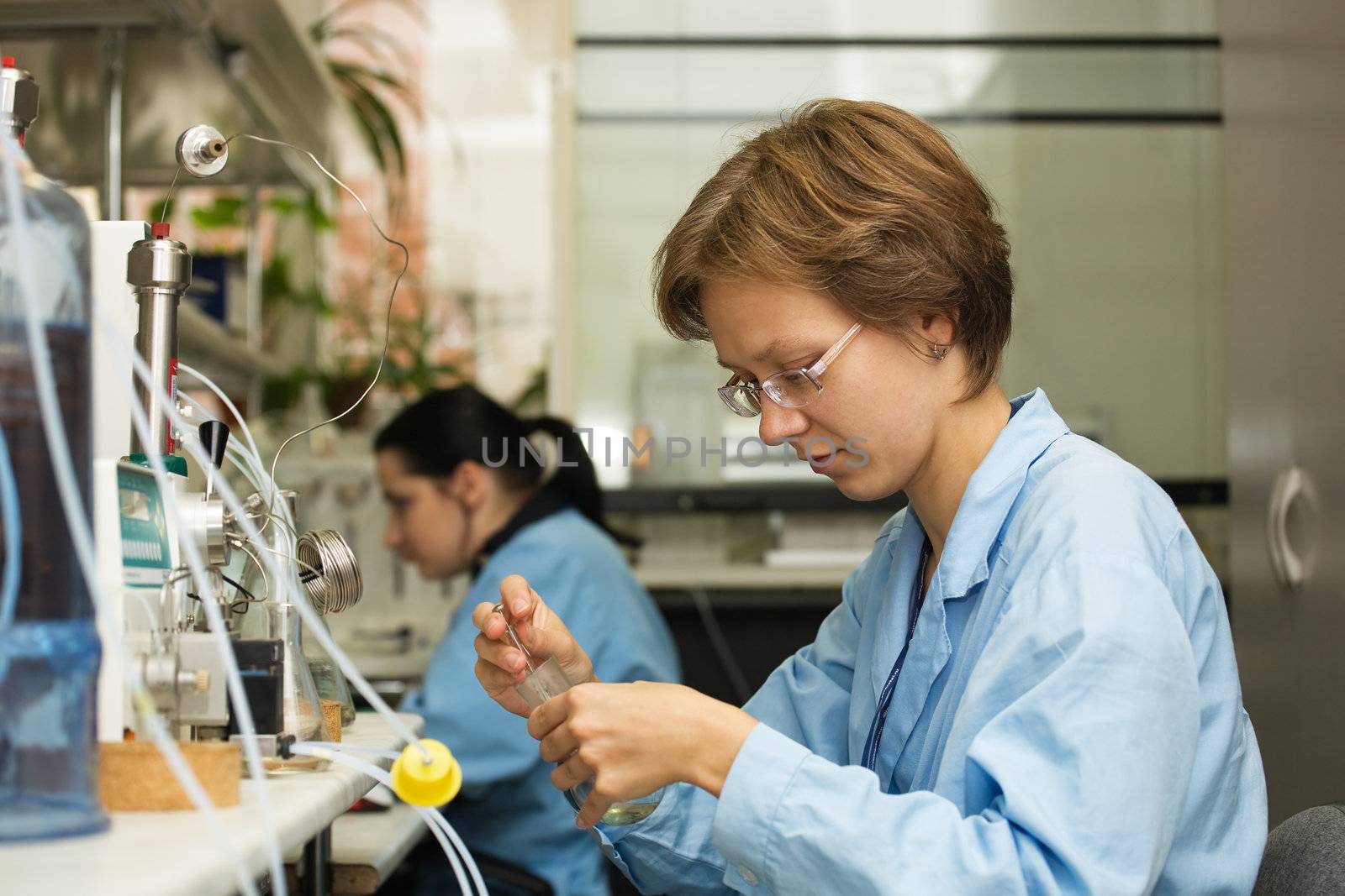 The young nice woman-scientist work with syringe on a background scientific instruments